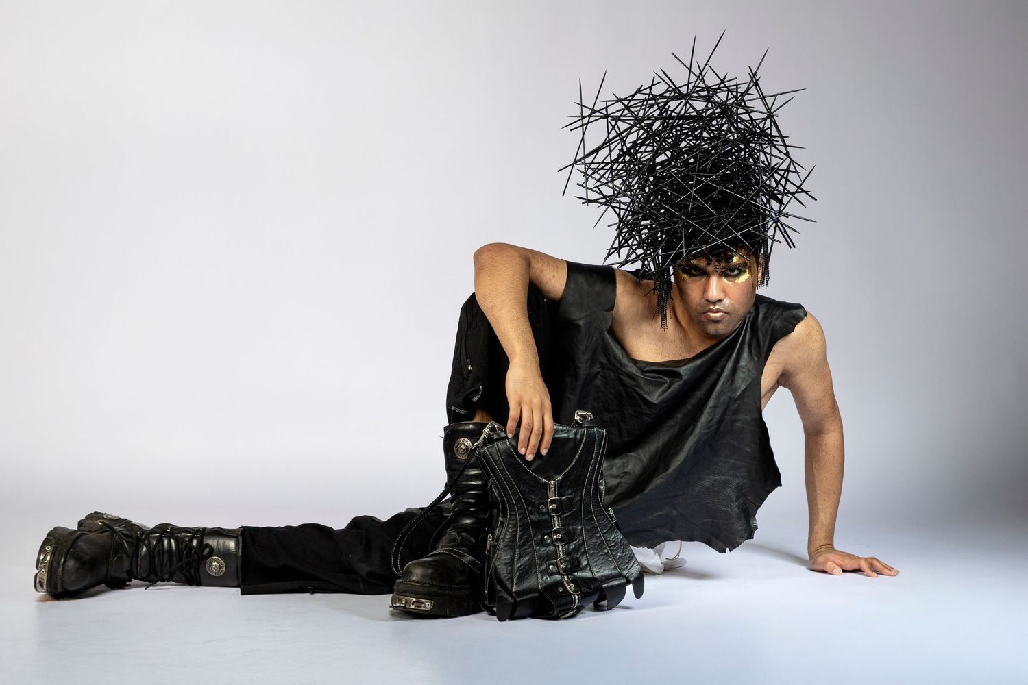 Model in edgy black outfit with dramatic spiked headpiece poses on floor in avant-garde fashion shoot.