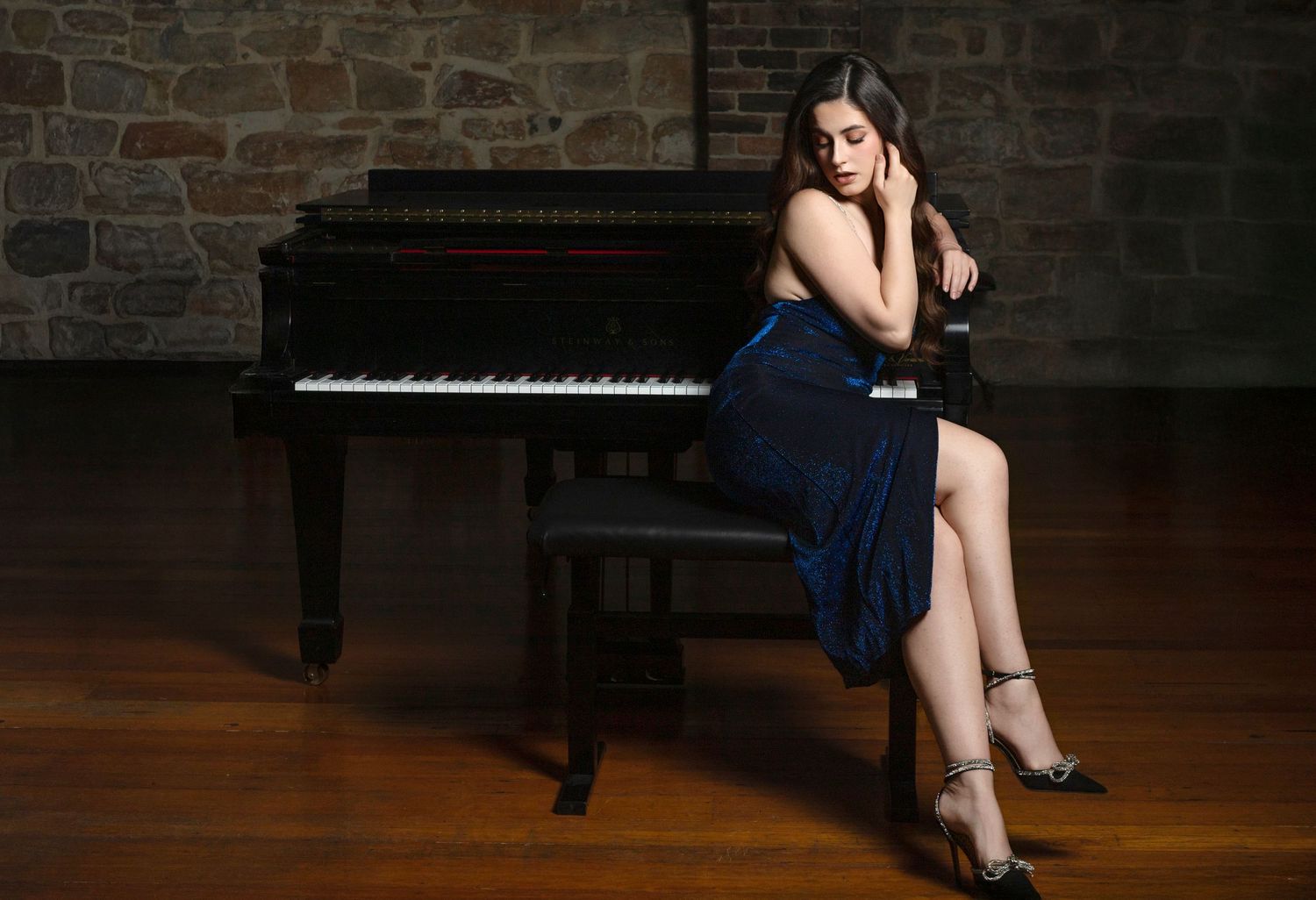 Woman in blue dress seated at a grand piano in an elegant stone-walled room.