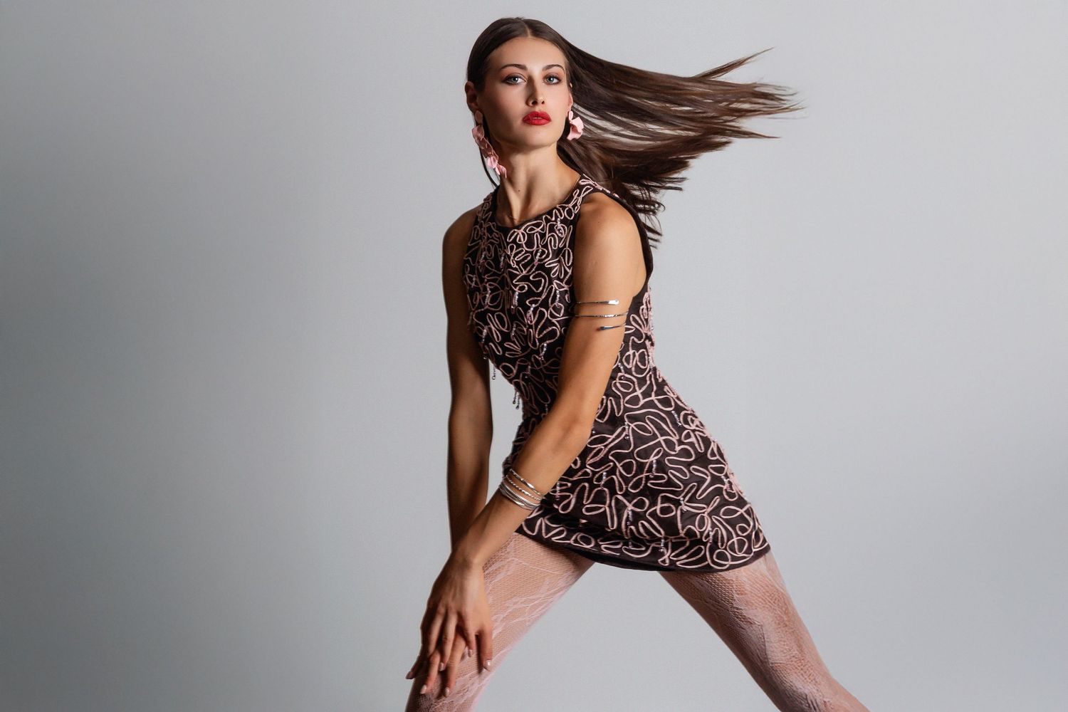 Woman in patterned mini dress posing dynamically with hair flowing, against a light gray background.