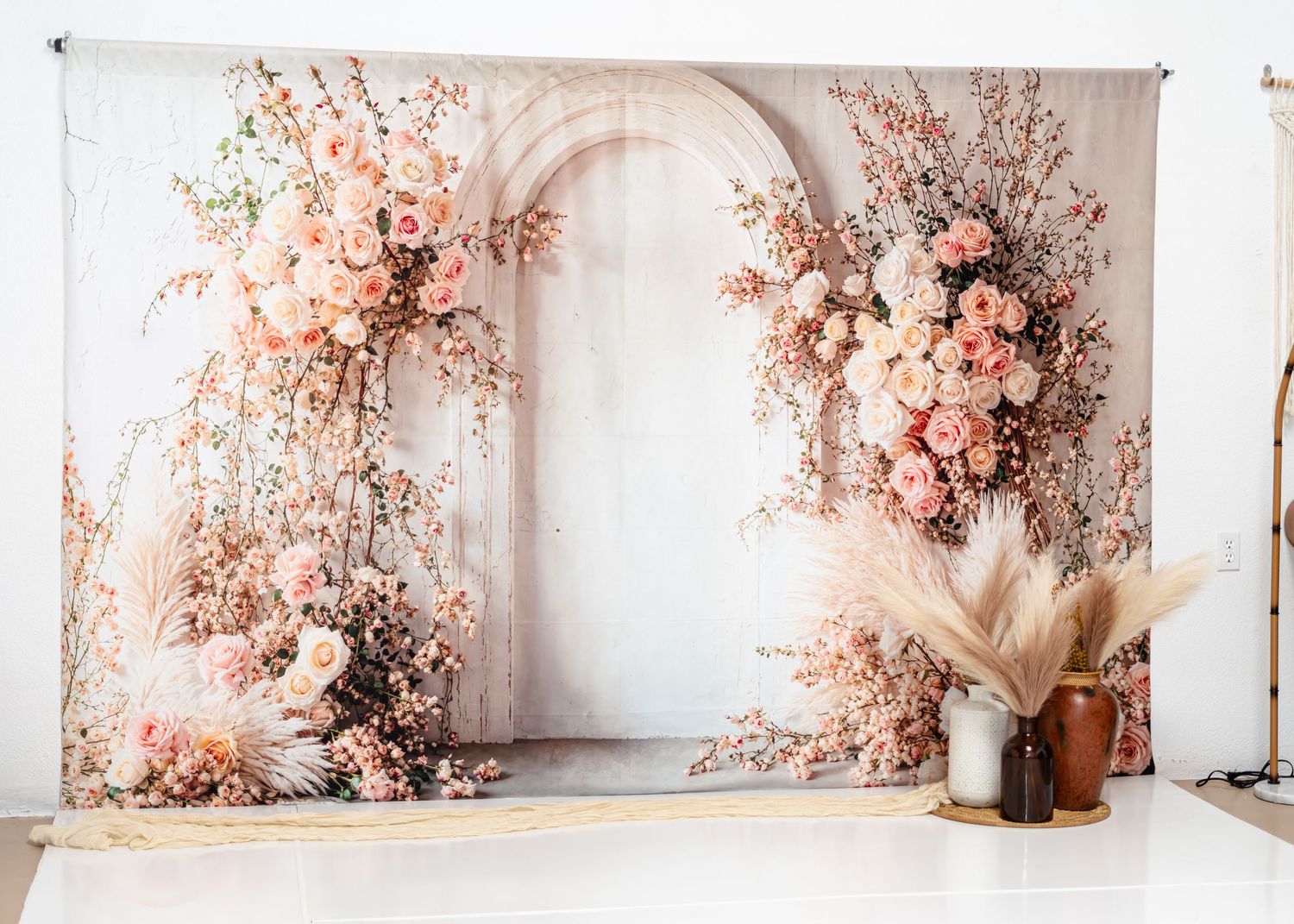 Floral arch photography backdrop with pink roses and dried pampas grass in studio setting.