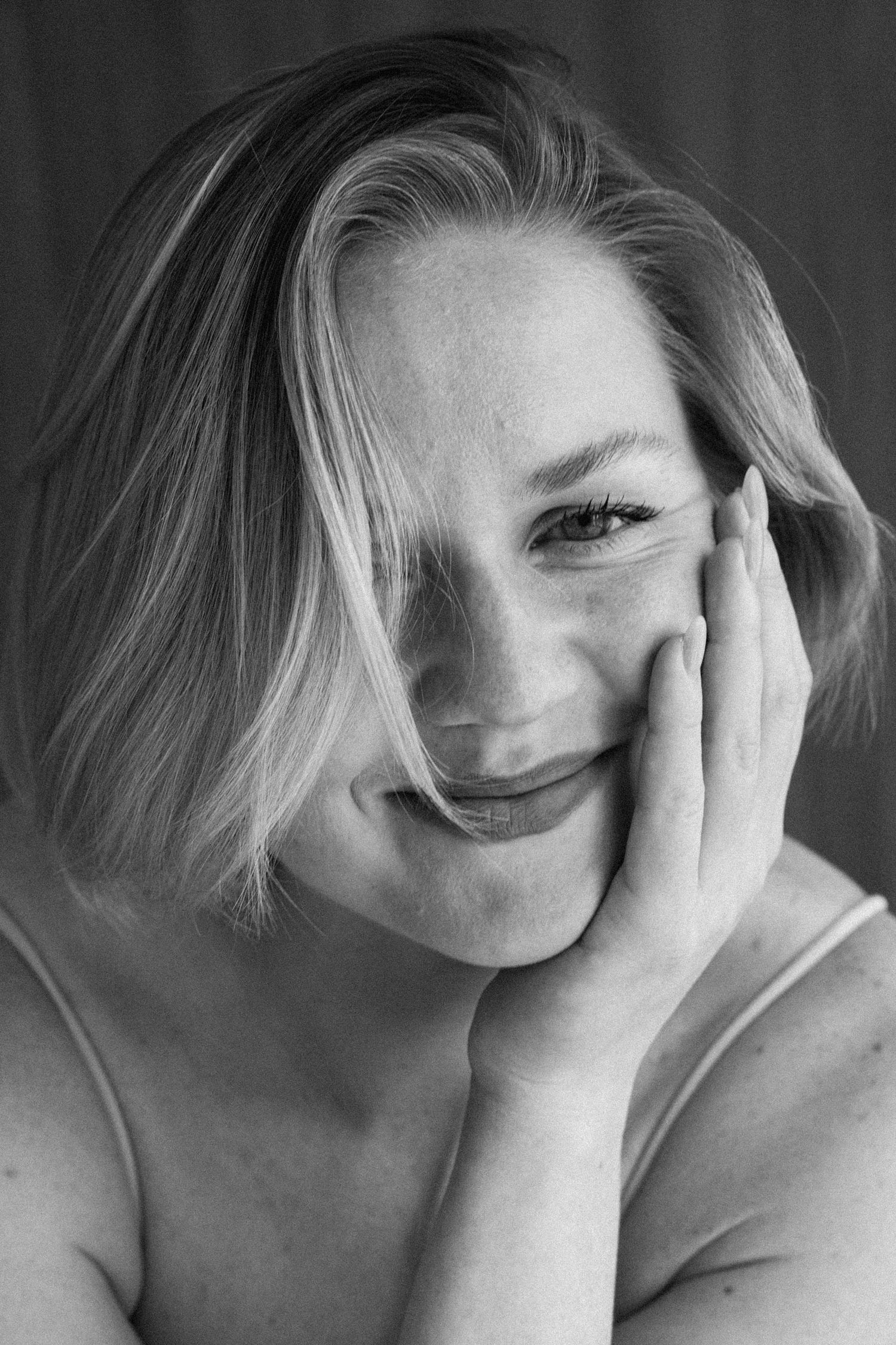Black and white portrait of a smiling blonde woman with freckles, resting her cheek on her hand.