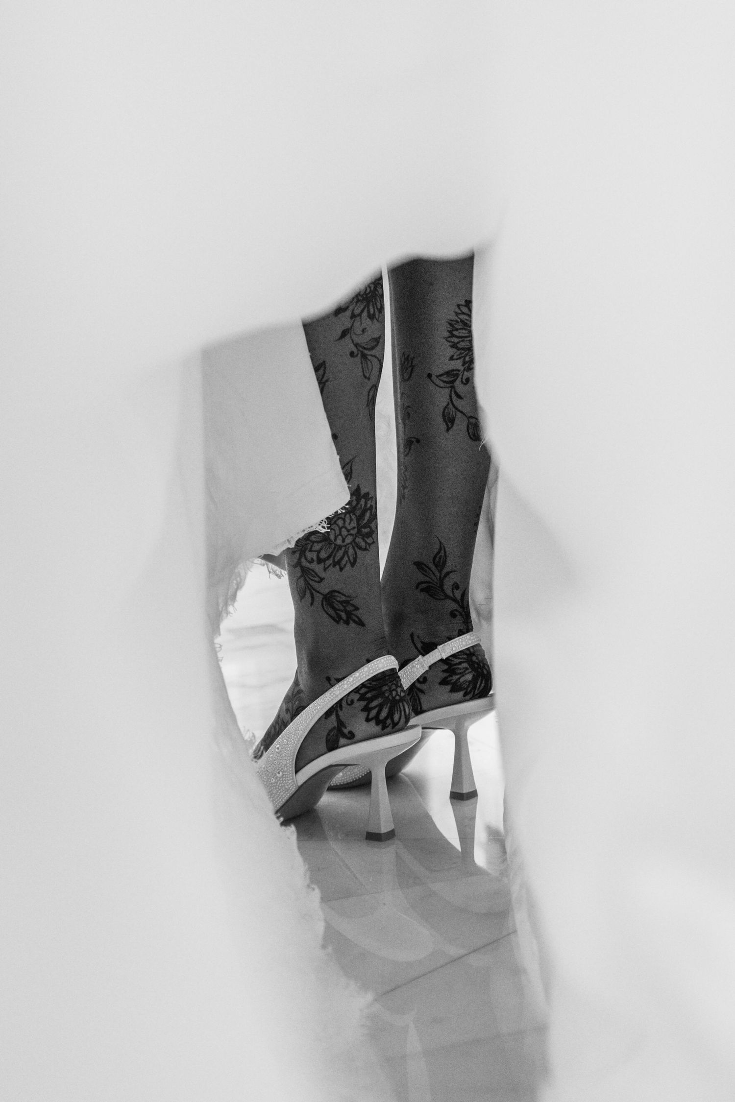 Black and white photo of floral patterned high-heel boots viewed through a torn paper hole.