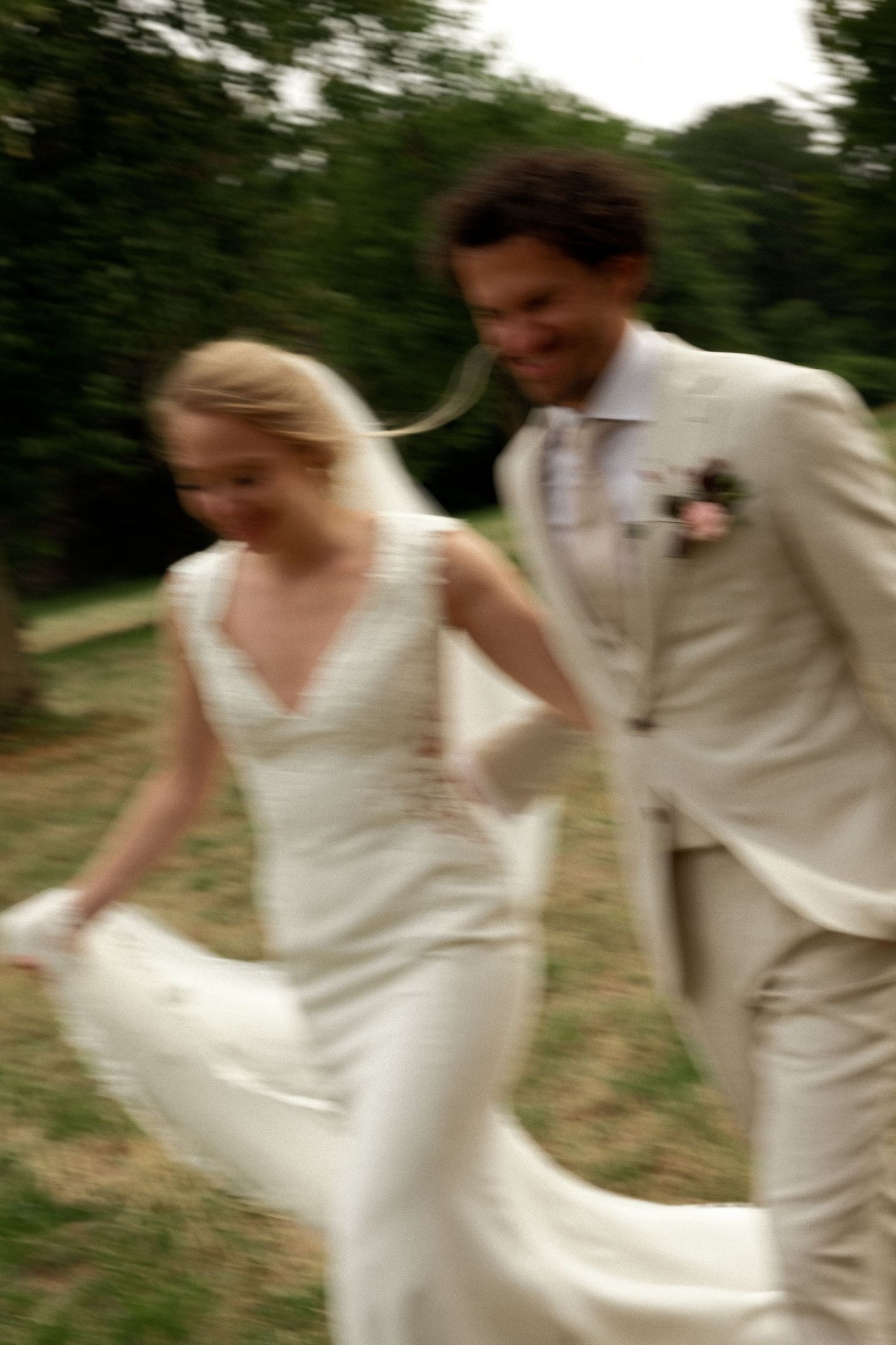 Blurred motion photo of happy bride and groom running together through a lush green garden.