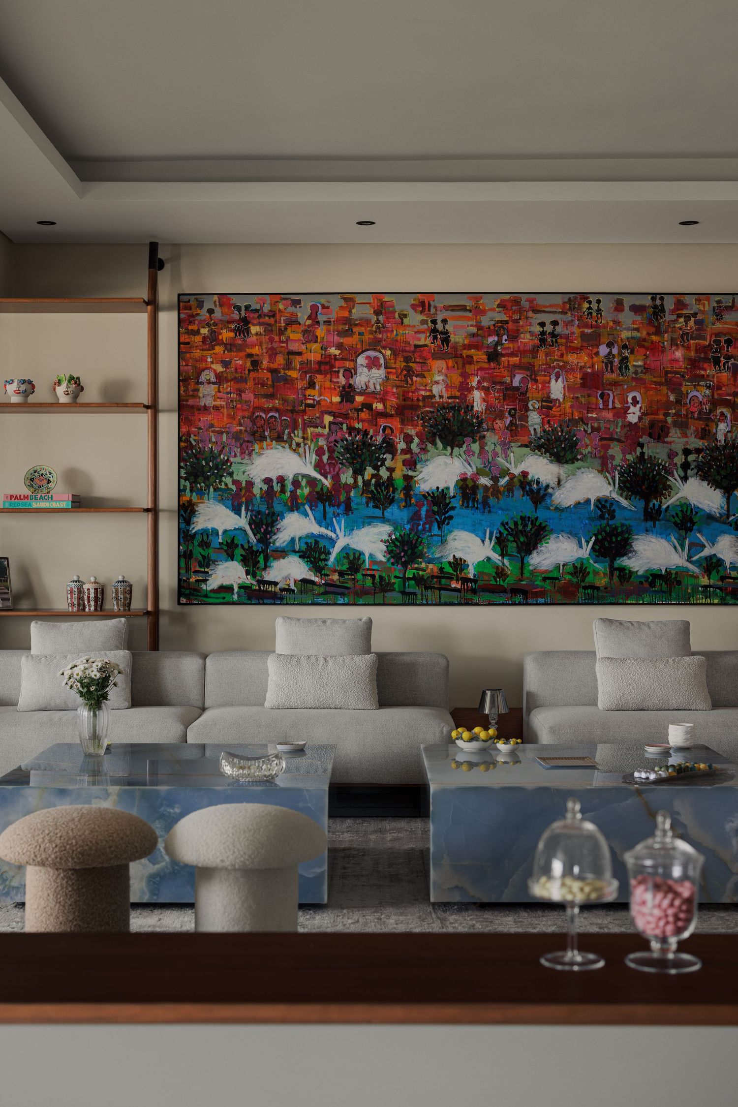 Modern living room with gray sectional sofa, large colorful cityscape painting, wooden shelves, and blue marble table.