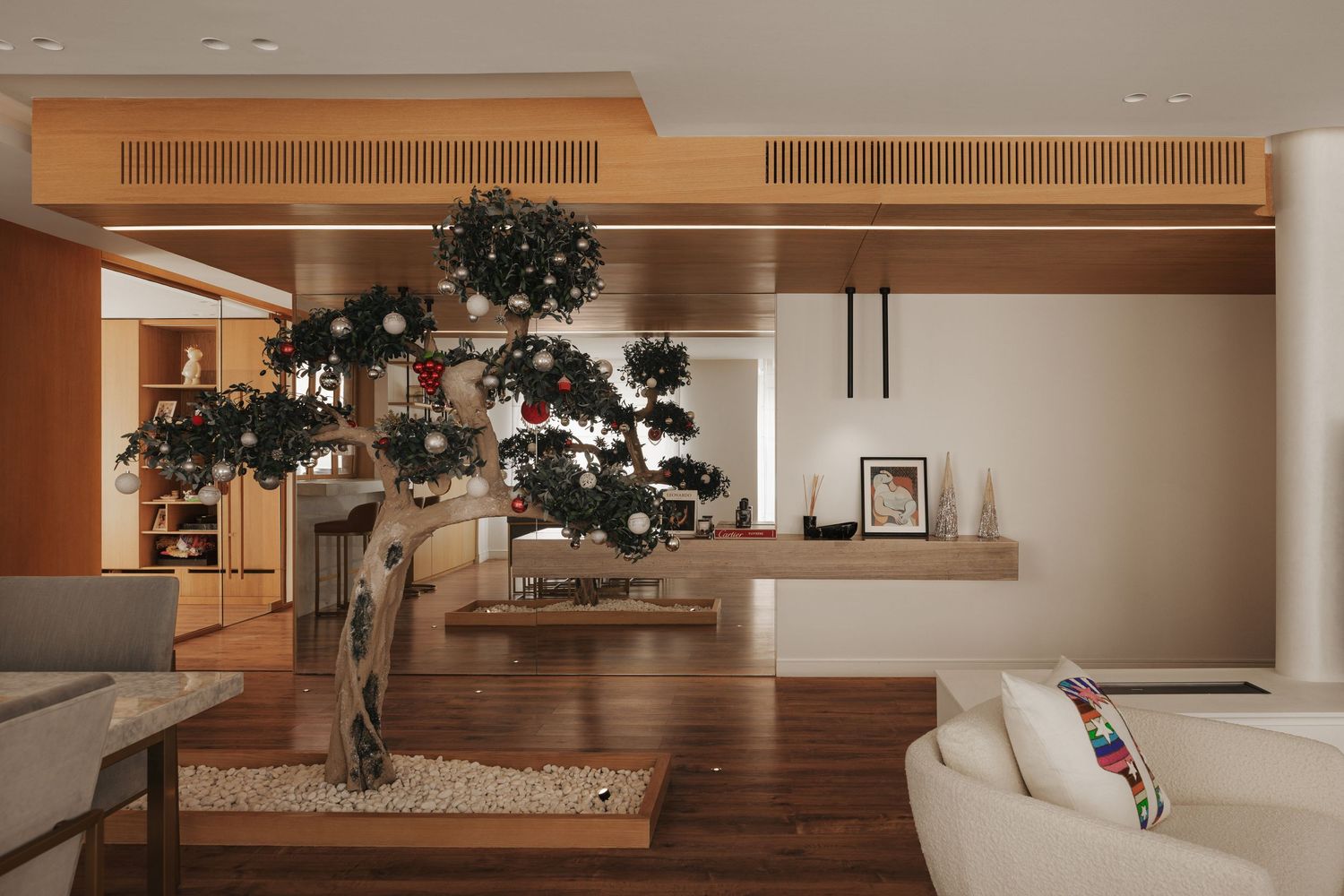 Elegant interior with ornate bonsai tree centerpiece, white pebble base, wooden ceiling detail, and wall-mounted TV unit.