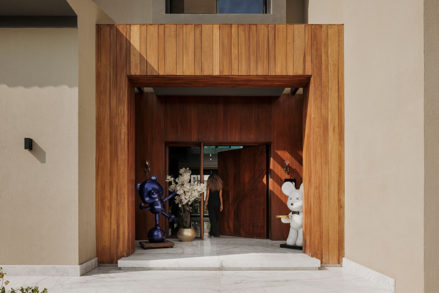 Modern home entrance with warm wood cladding, double doors, and decorative sculptures flanking the entryway.