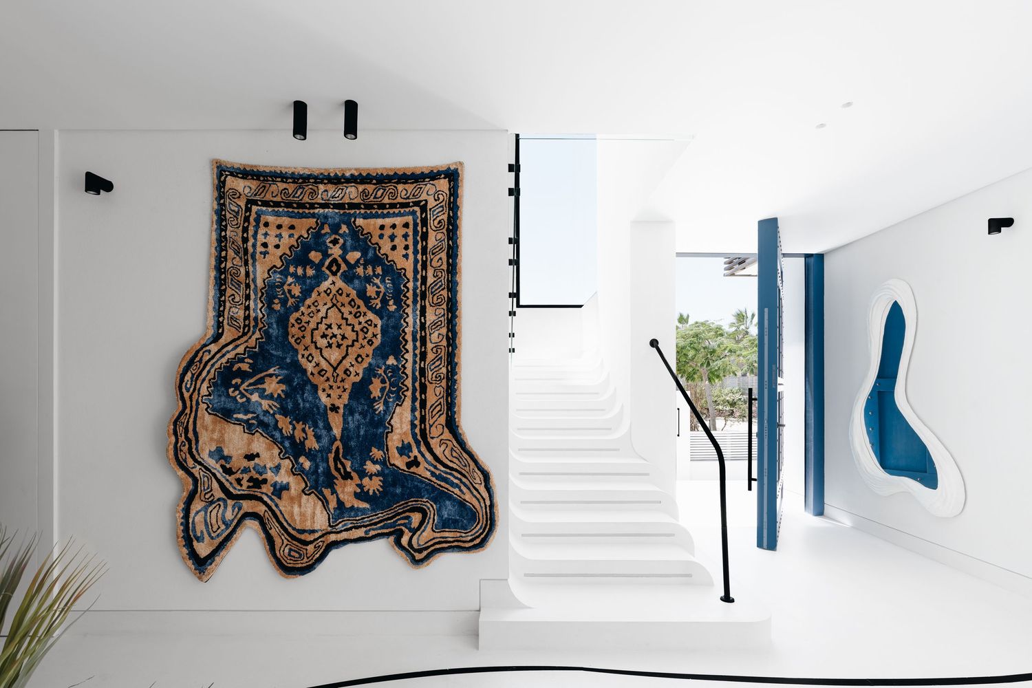 Modern white entryway featuring a decorative Persian rug wall hanging and abstract blue artwork beside a staircase.