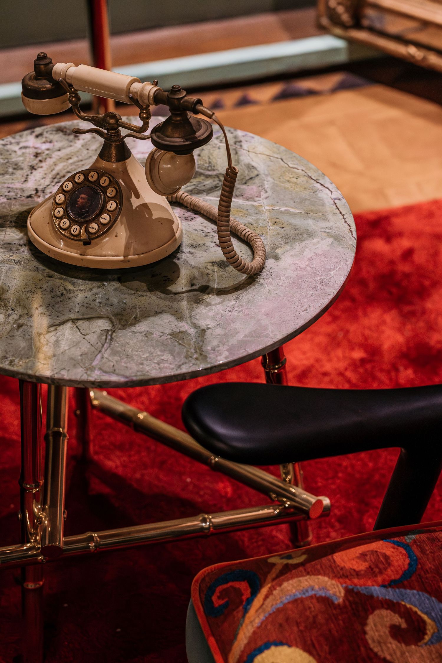 Vintage rotary telephone on marble-top brass side table with red patterned carpet in retro interior setting.