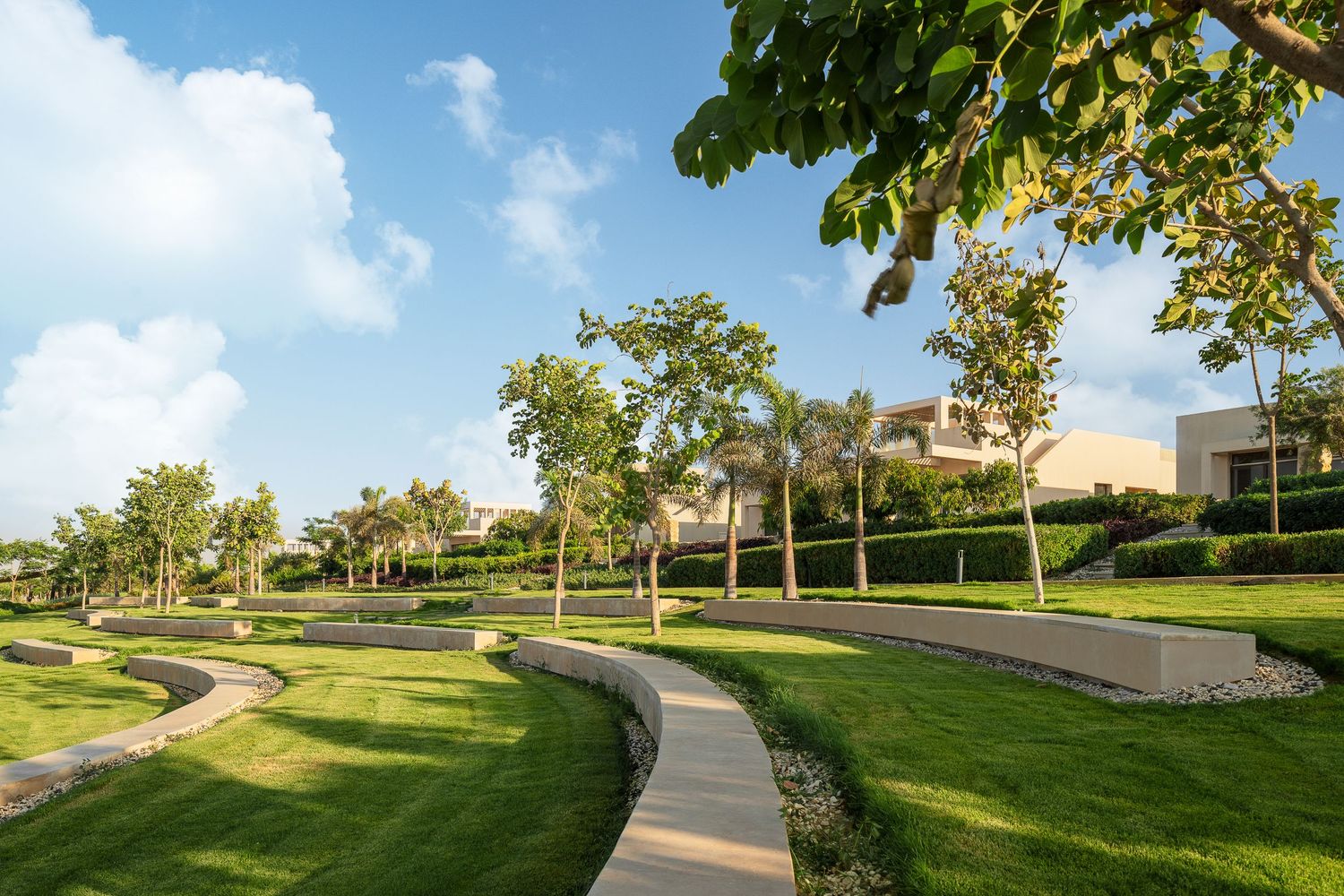 Manicured green lawns with winding pathways, mature trees, and elegant residential villas in a upscale community.