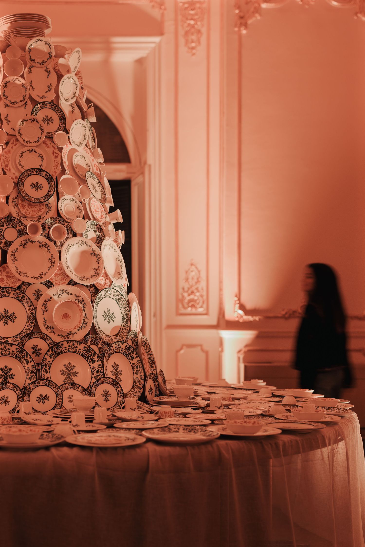 Elegant china plates displayed on a tiered stand in a grand room with warm pink ambient lighting.