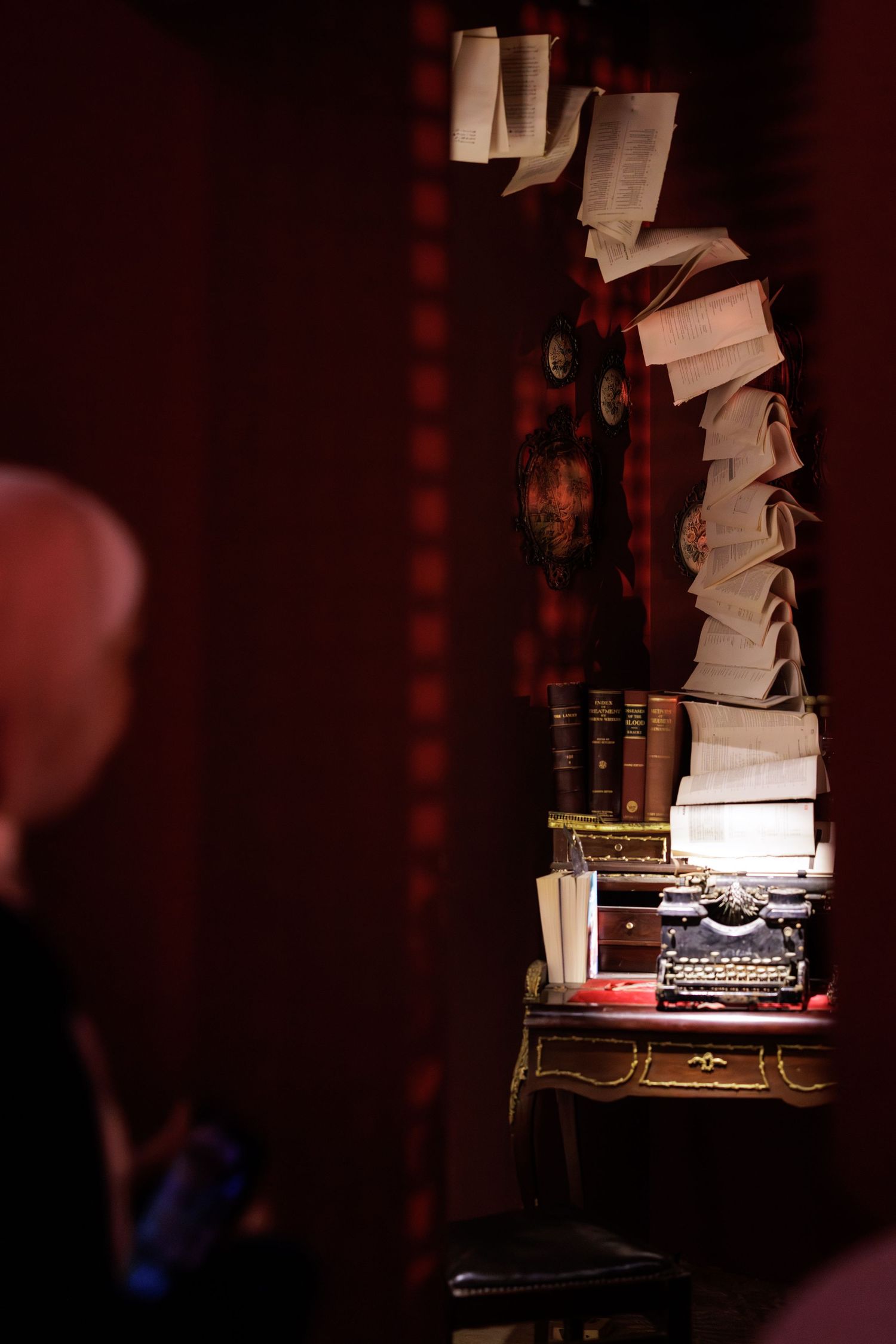 Vintage typewriter on antique desk with floating papers and old books in a dimly lit red room.