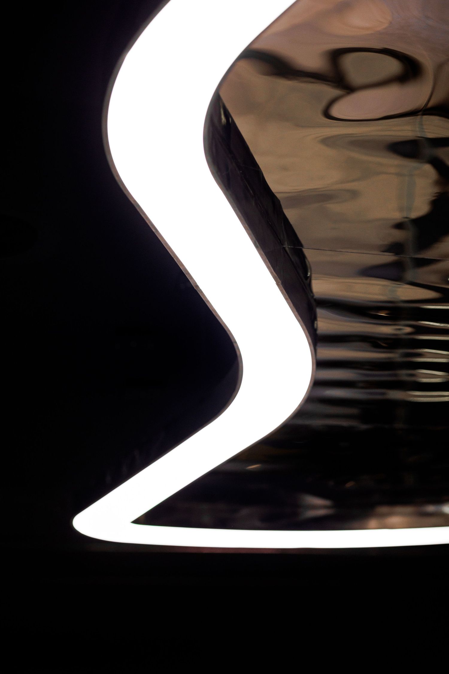 Glowing white neon light in S-curve shape against dark reflective surface.