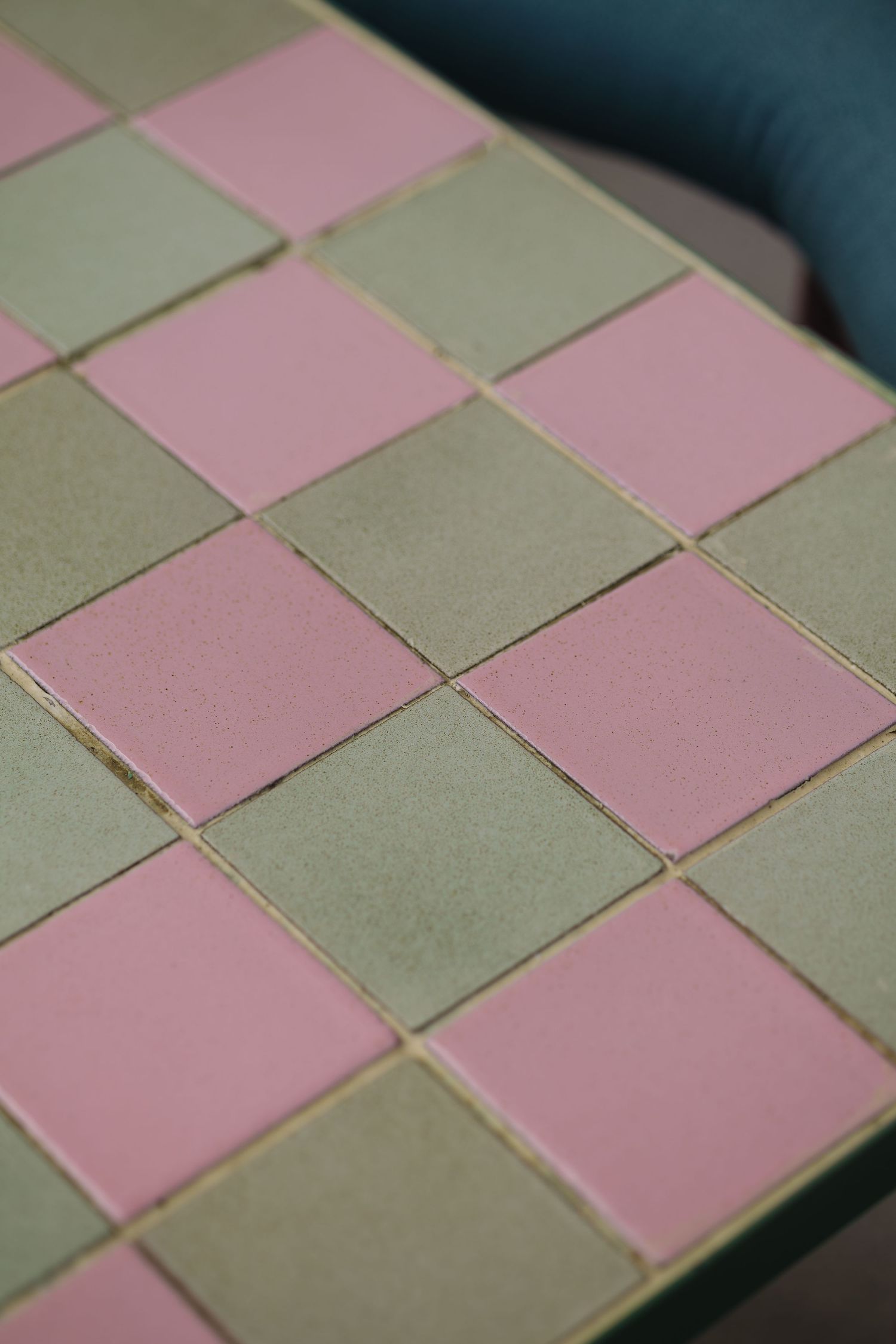 Close-up of a checkerboard tile surface with alternating pink and sage green square tiles.