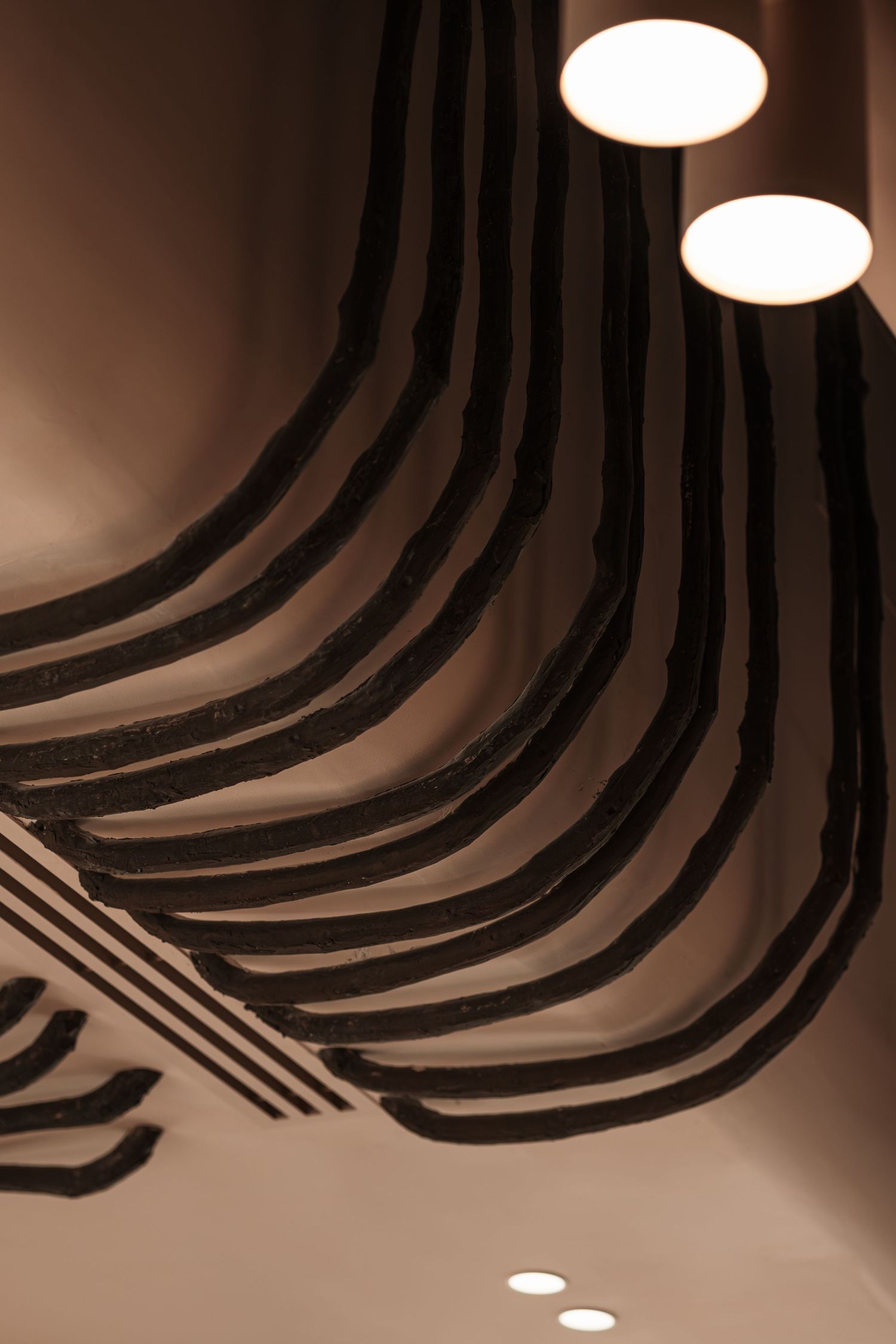 Dark wavy ceiling installation with round glowing pendant lights in a modern interior.