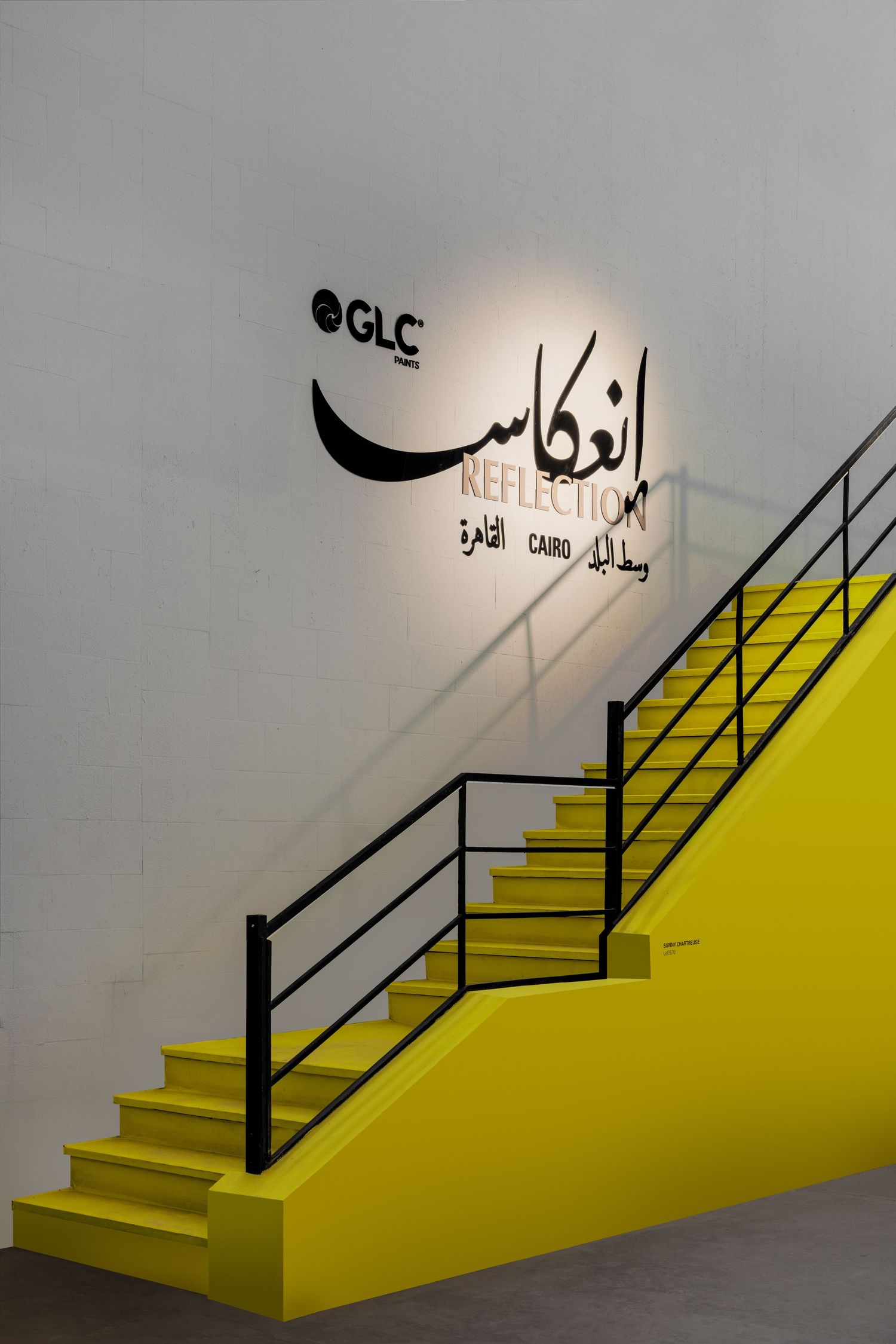 Bright yellow staircase with black railing beneath a GLC Reflection Cairo exhibition sign.