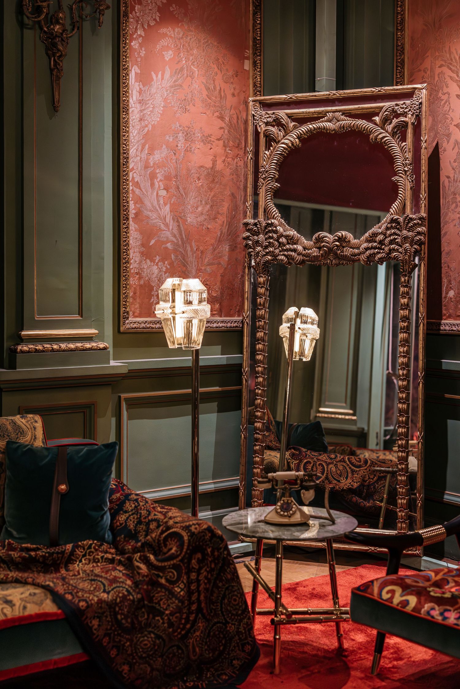 Opulent Victorian room with ornate gilded mirror, crystal floor lamp and rich red damask walls.
