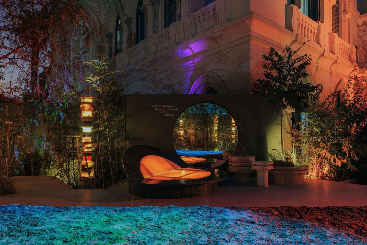 Colorful nighttime garden installation with glowing orange daybed, arch, and vibrant purple and teal lighting.