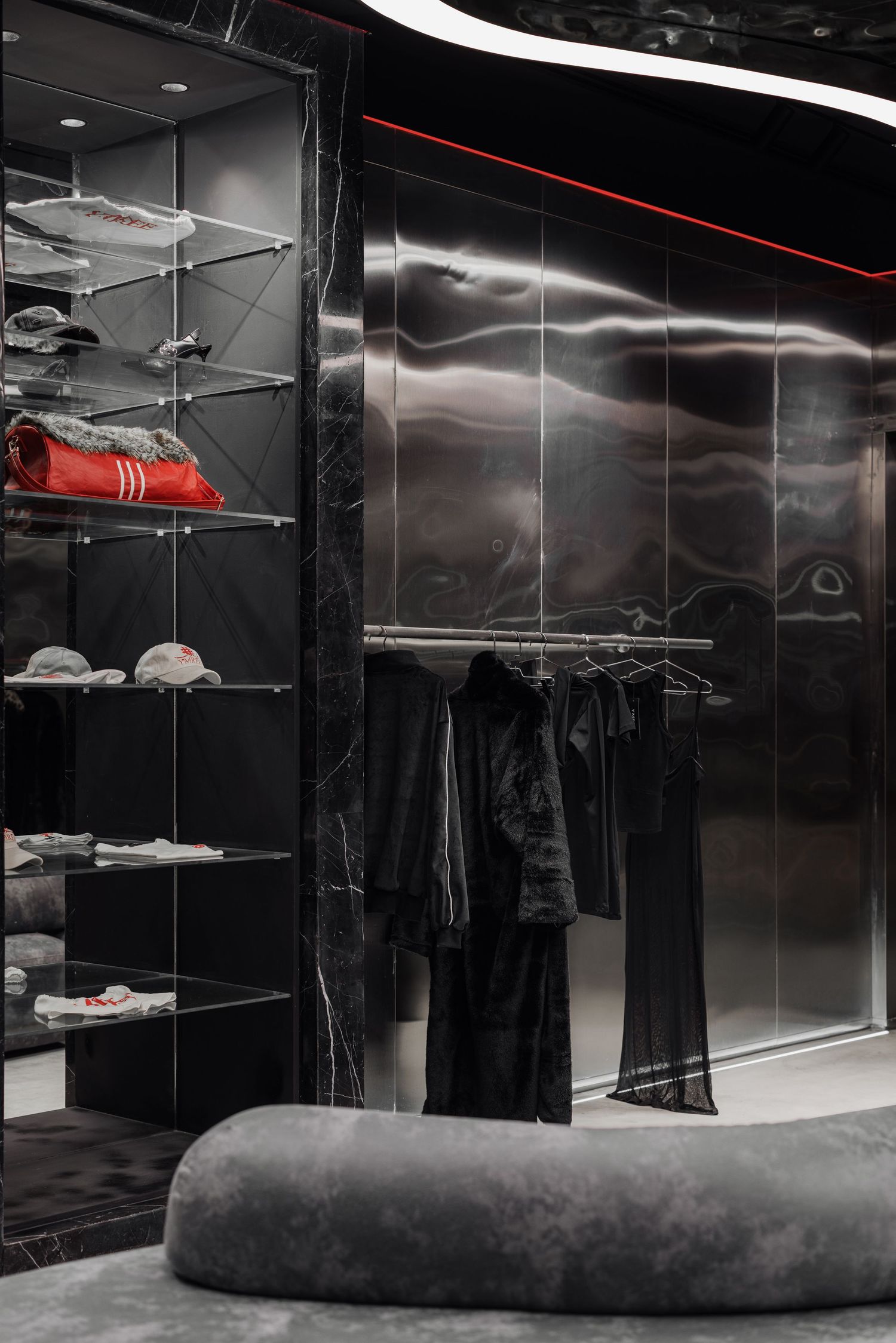 Luxury fashion store corner with black marble shelving, glass display shelves with sneakers, and dark clothing rack.