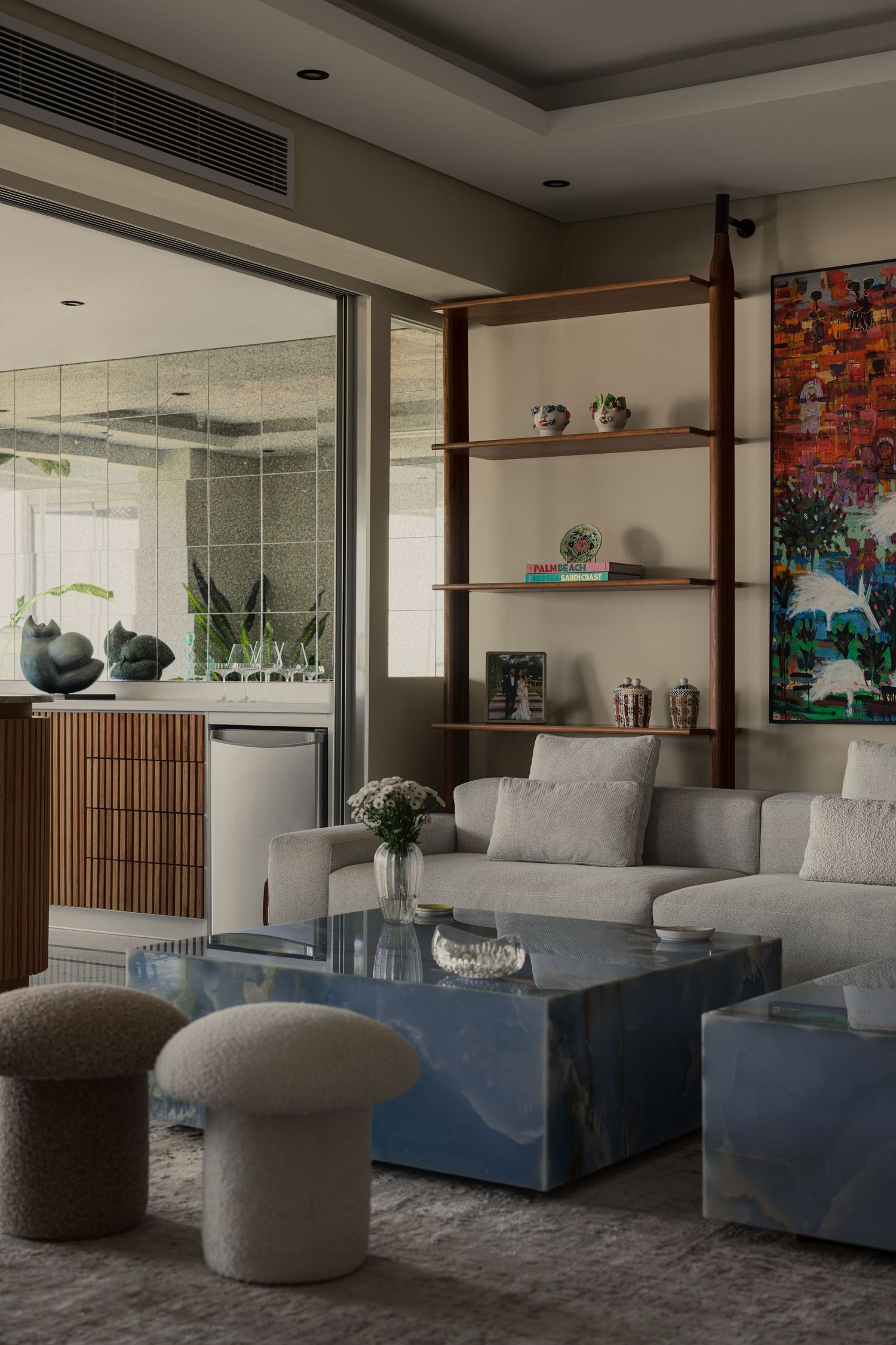 Modern living room with gray sofa, blue marble coffee table, wooden shelving unit, and colorful artwork on wall.