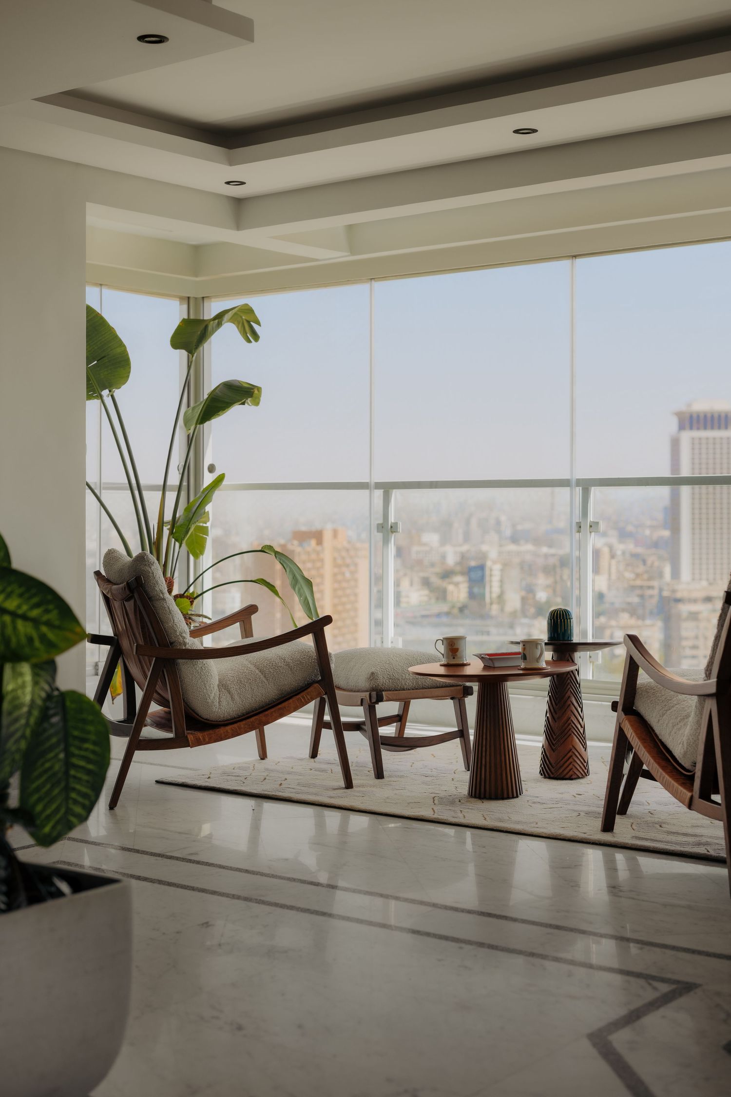 Stylish high-rise living room with mid-century wooden chairs, twisted side tables, and floor-to-ceiling city views.