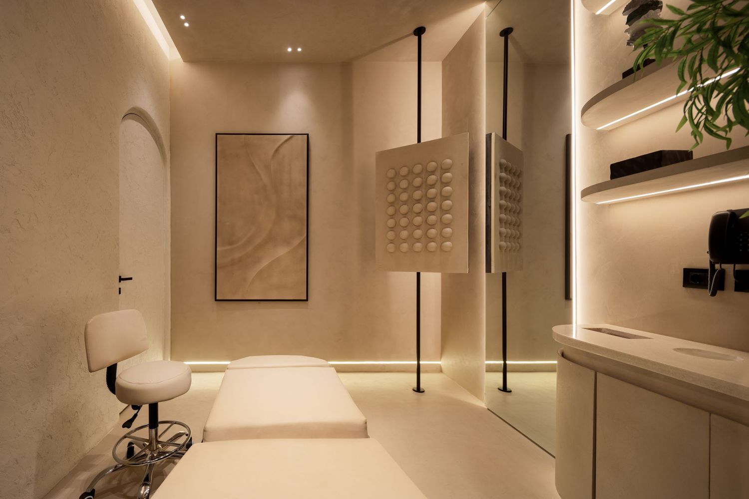 Serene spa treatment room with warm LED lighting, white massage table, shelving, and decorative wall art.