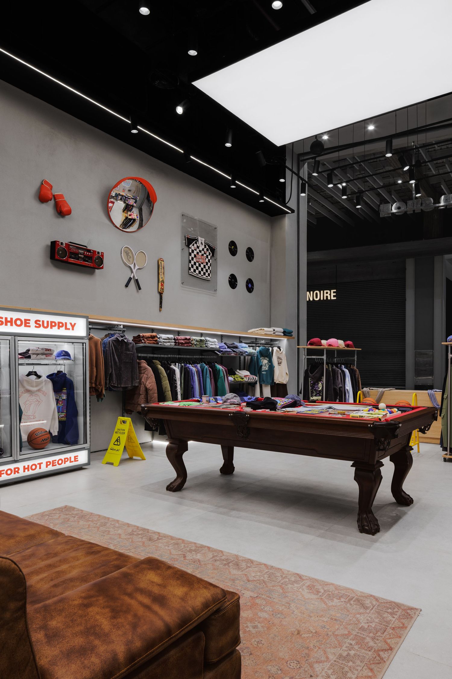 In Your Shoe Supply store interior with pool table, clothing racks, eclectic wall decorations, and a brown leather ottoman seating area.