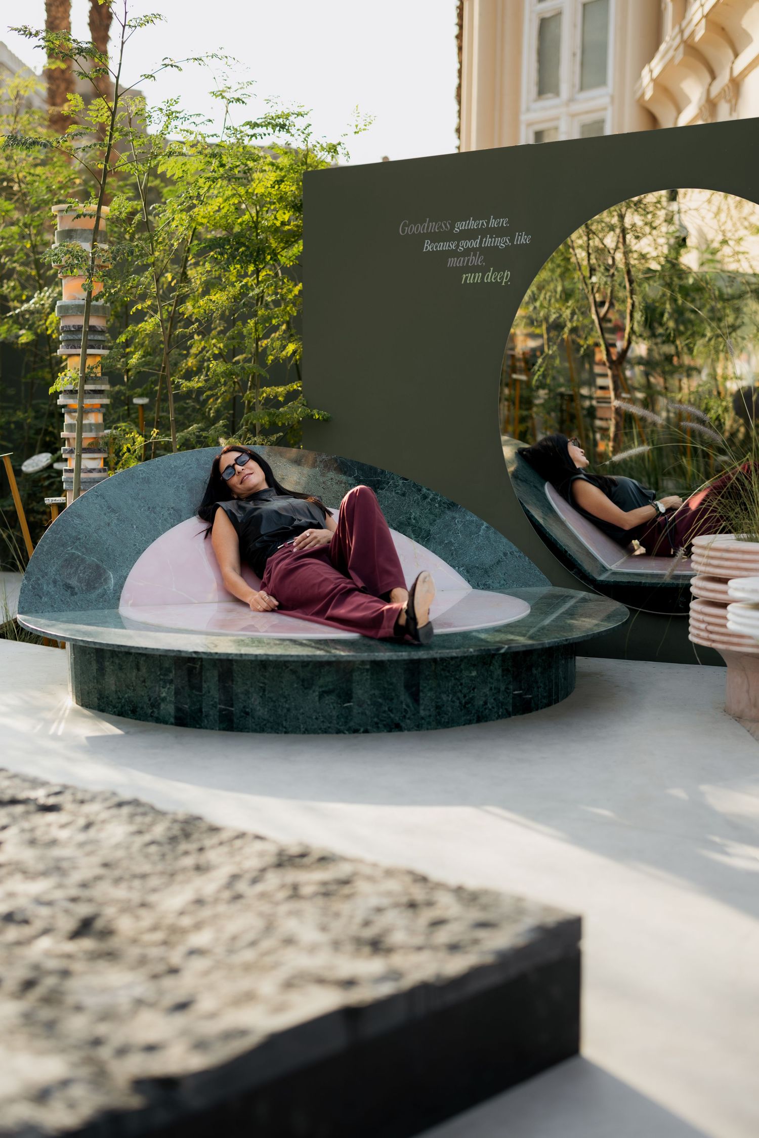 Woman relaxing on a luxurious green marble outdoor daybed with pink cushion in a modern garden setting.