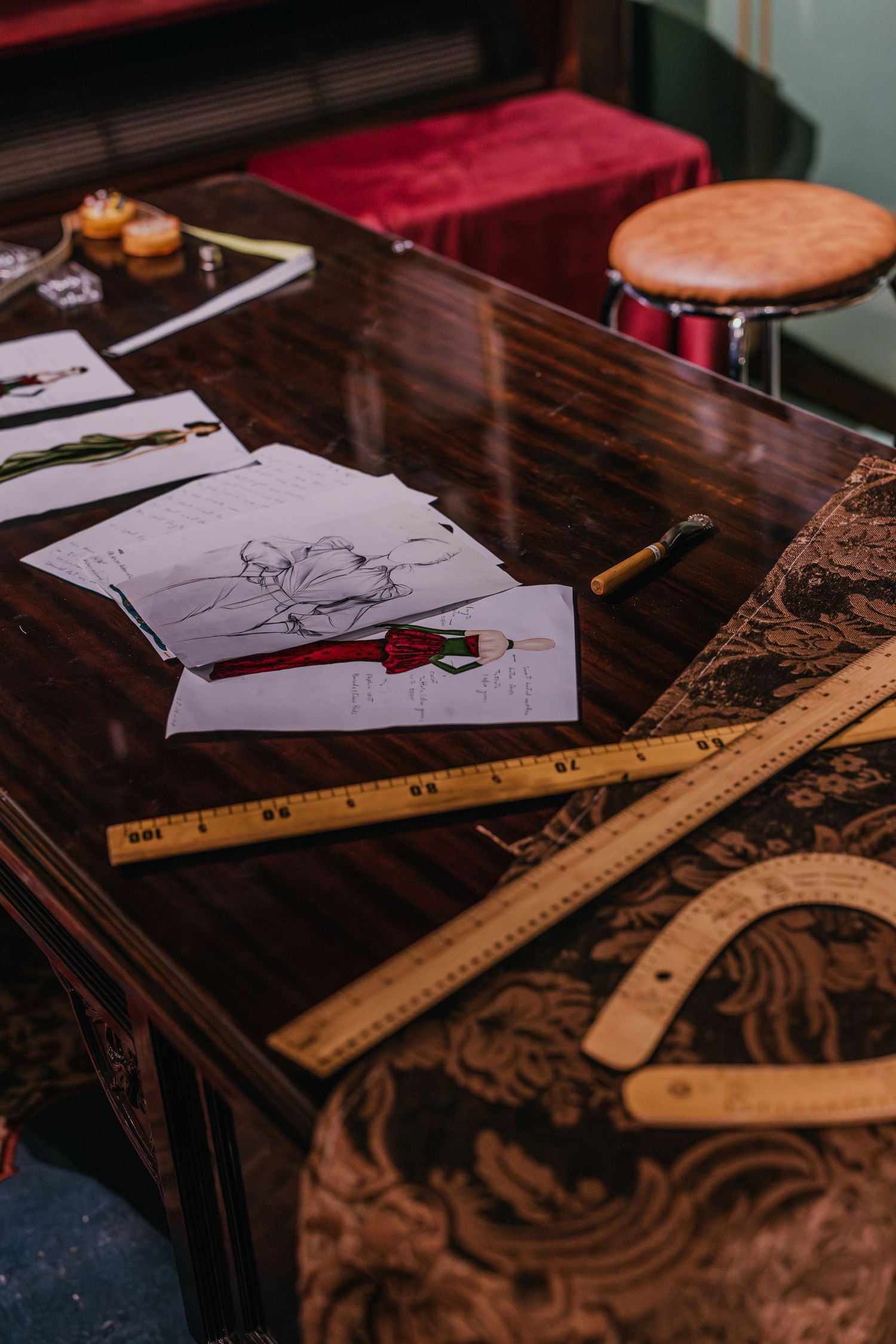 Fashion design sketches and wooden rulers on dark polished desk in a luxury atelier workspace.