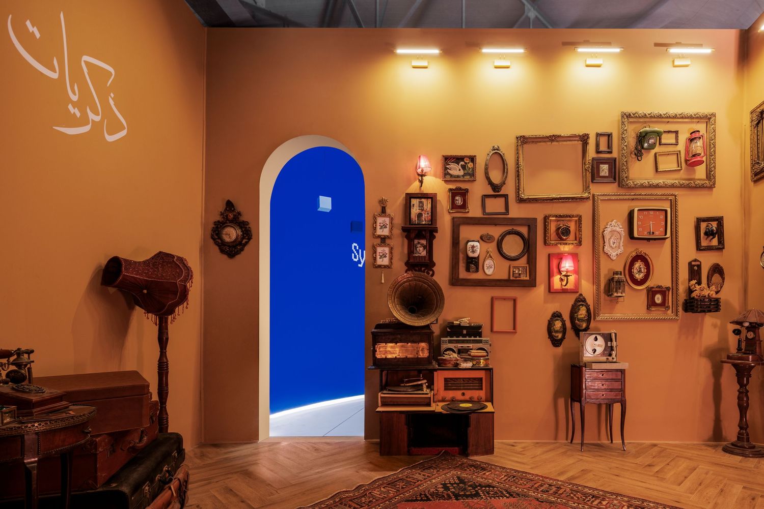 Warm orange room with Arabic script, blue arched door, antique clocks, and framed artwork wall.