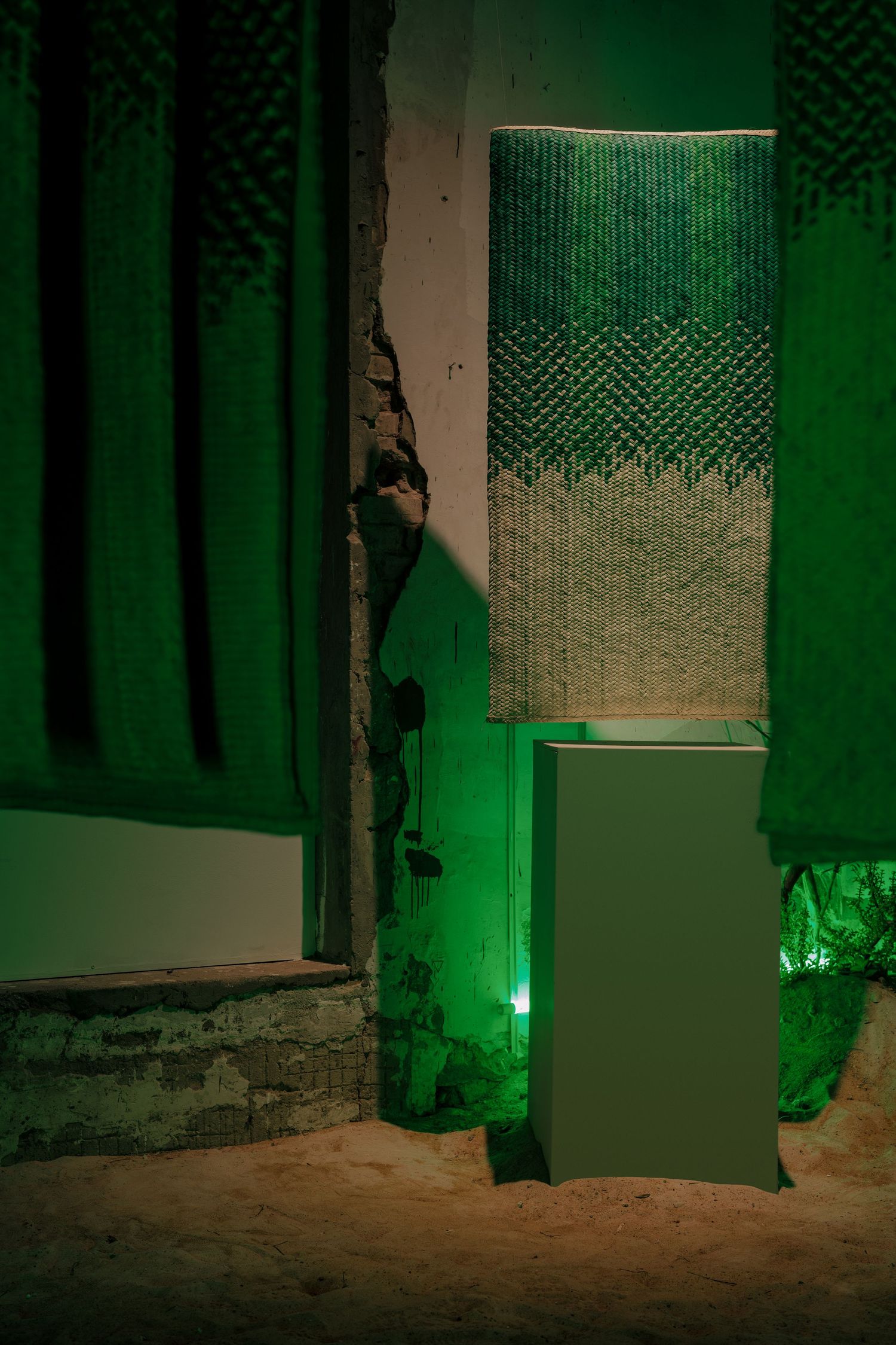 Dramatic installation with emerald green textured fabric panels and glowing green light against weathered concrete walls.