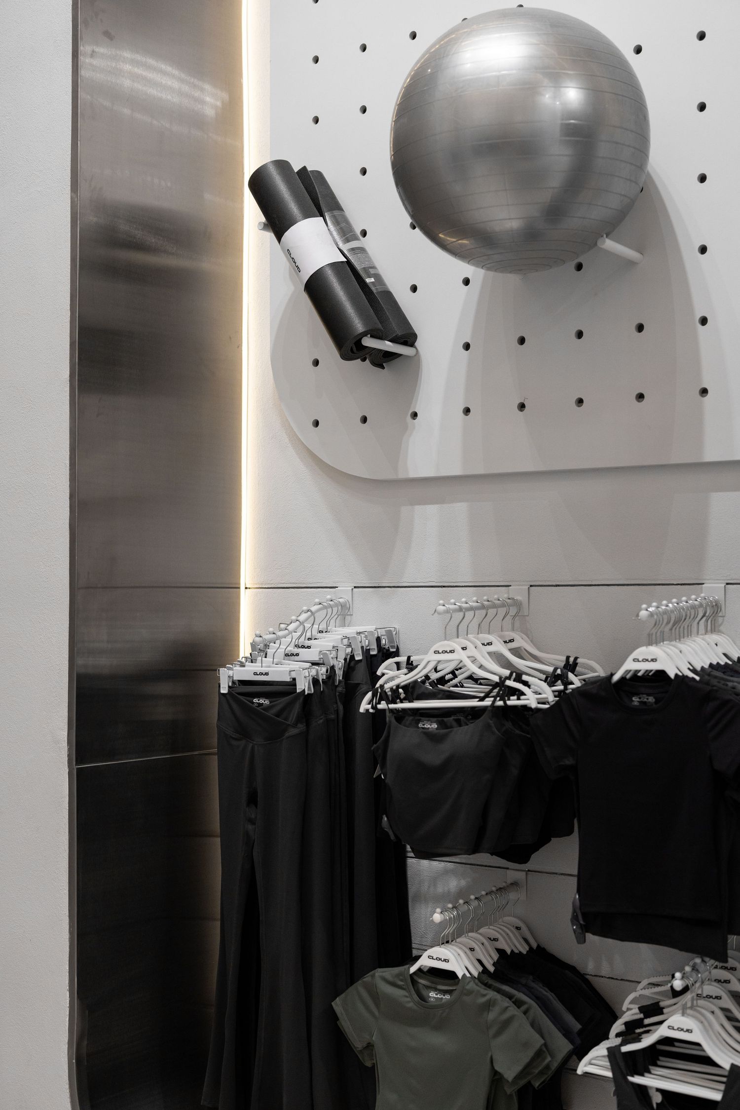 Athletic wear retail display with silver exercise ball and yoga mat on pegboard wall above clothing racks.