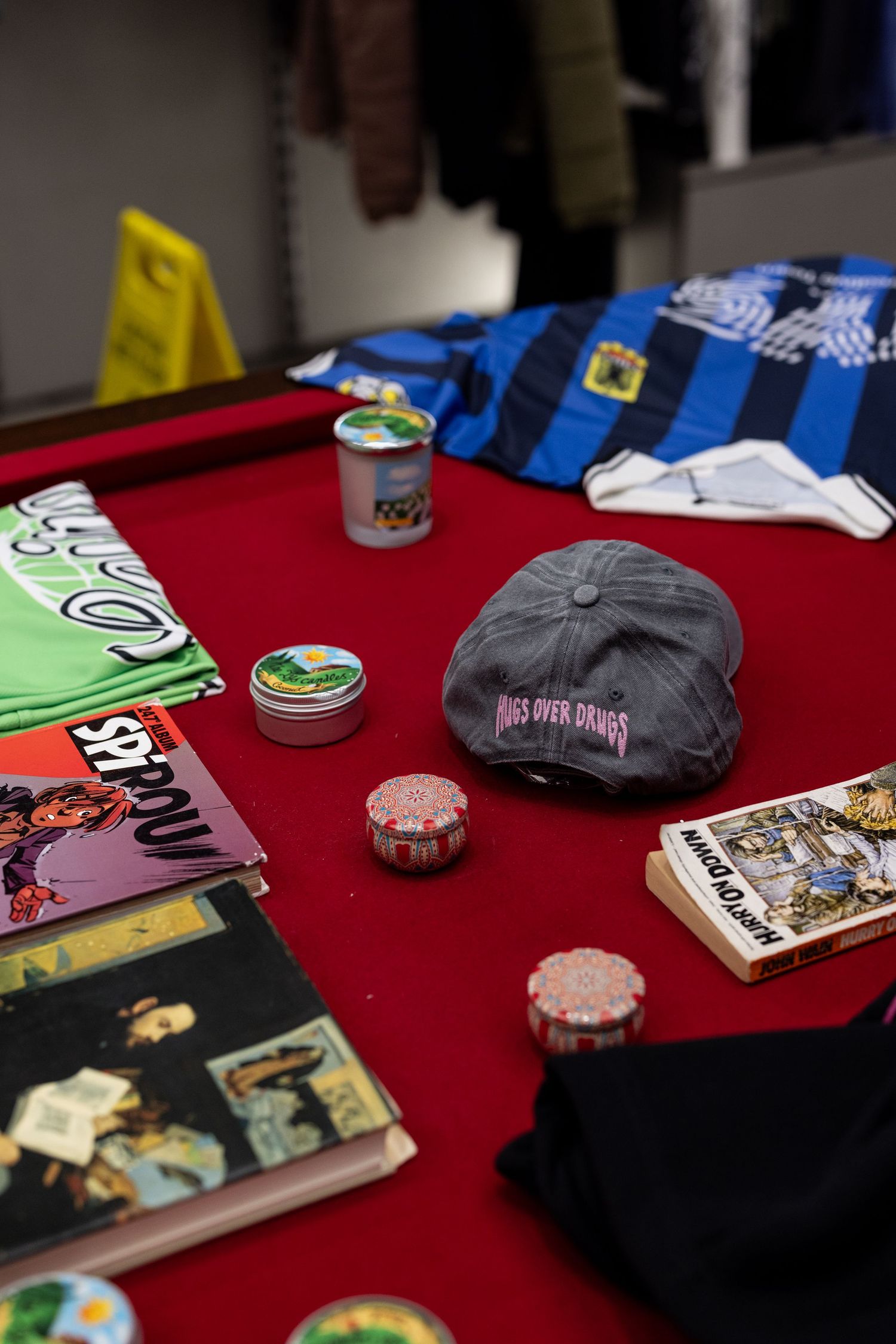 Red felt pool table displaying caps, tins, poker chips, magazines, and streetwear items in a store.
