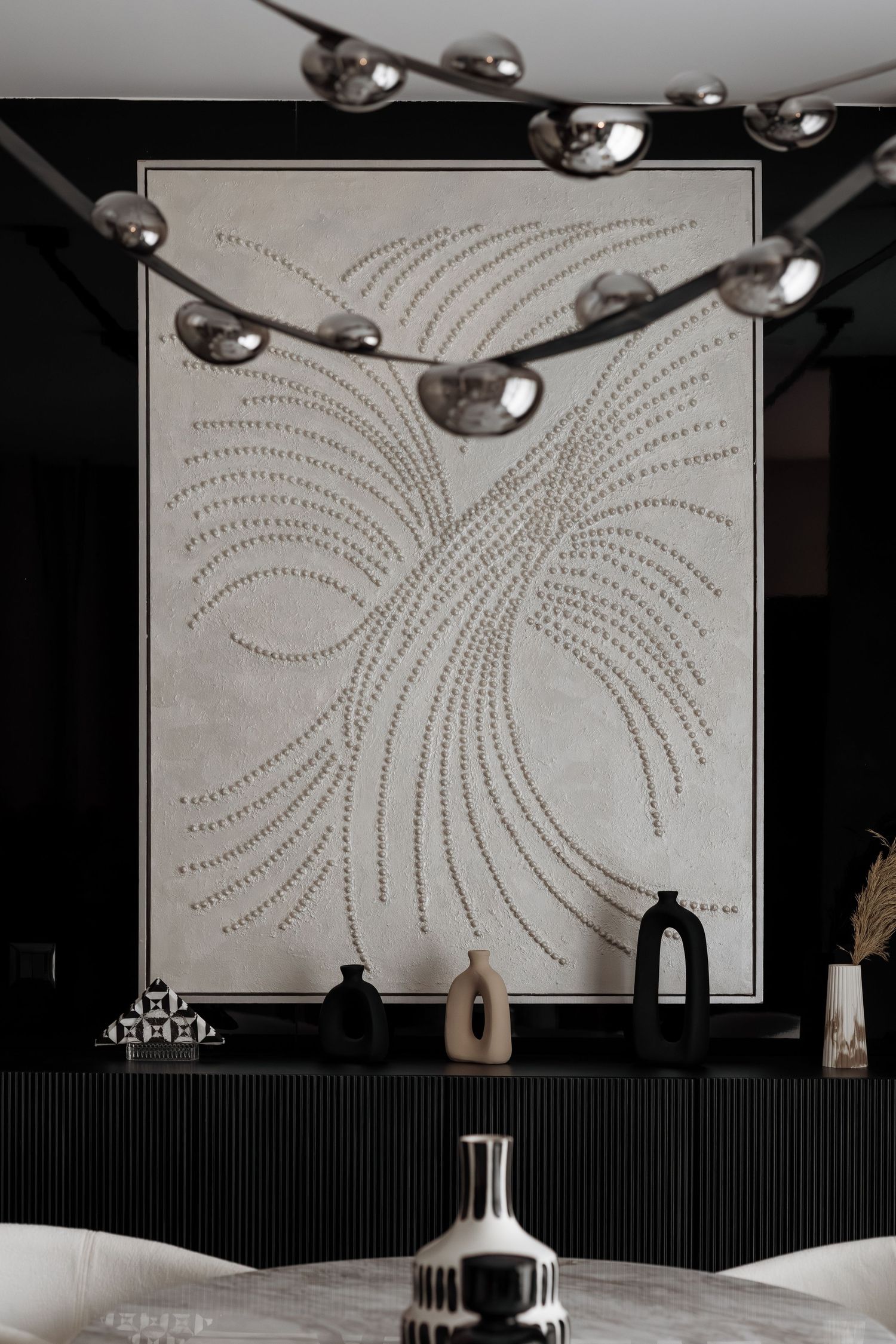Large botanical textured wall art above black sideboard with decorative vases and chandelier.