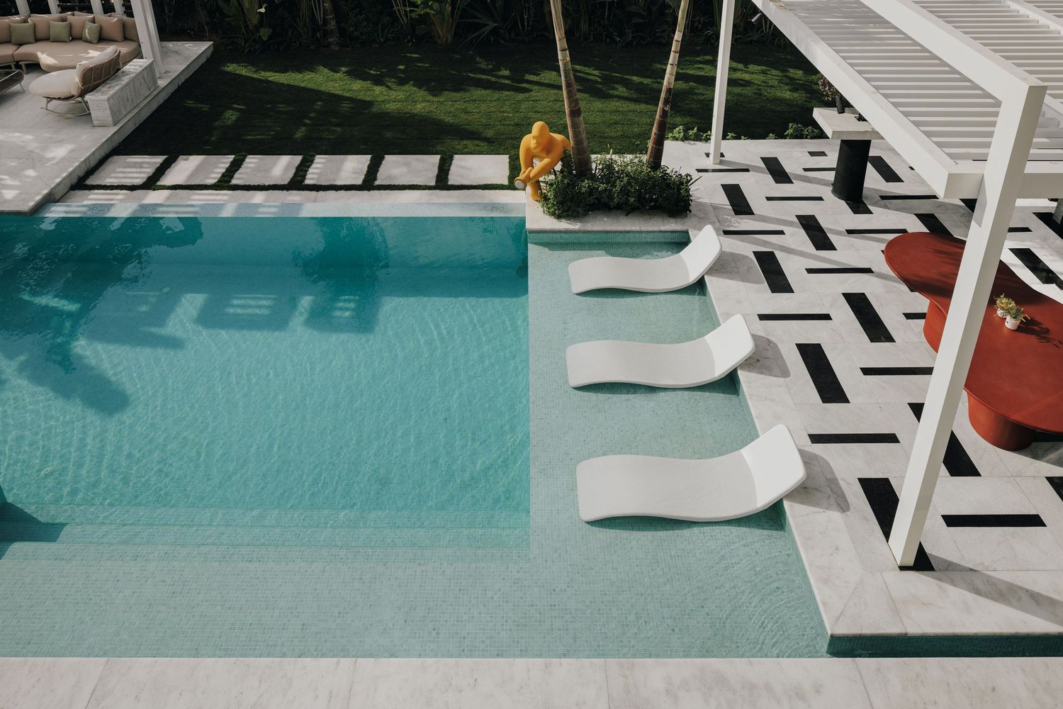 Aerial view of luxury pool with white sun loungers and bold geometric black and white tiles.