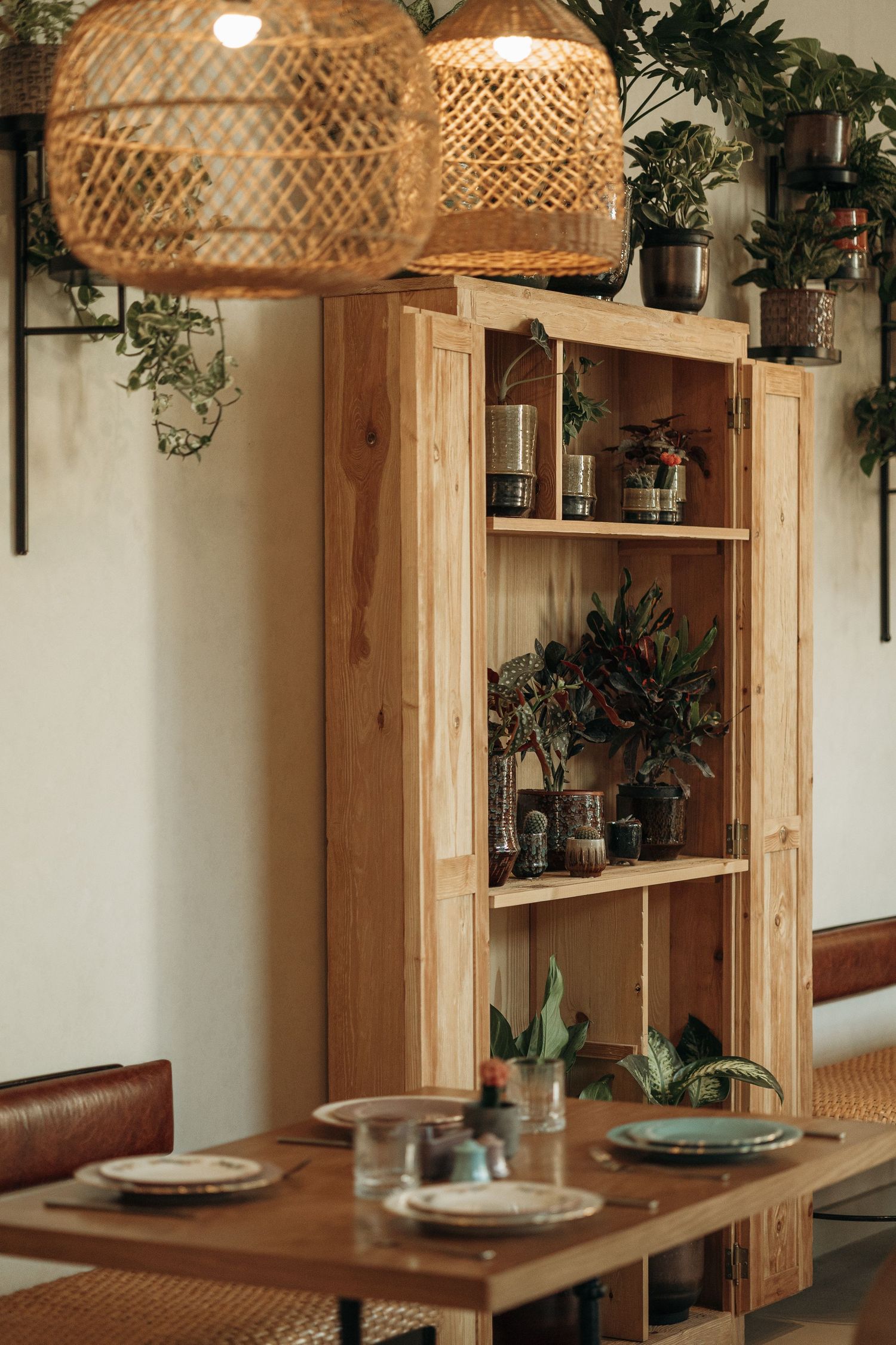 Rustic wooden bookshelf with plants and decor in a cozy cafe dining room with rattan pendant lights.