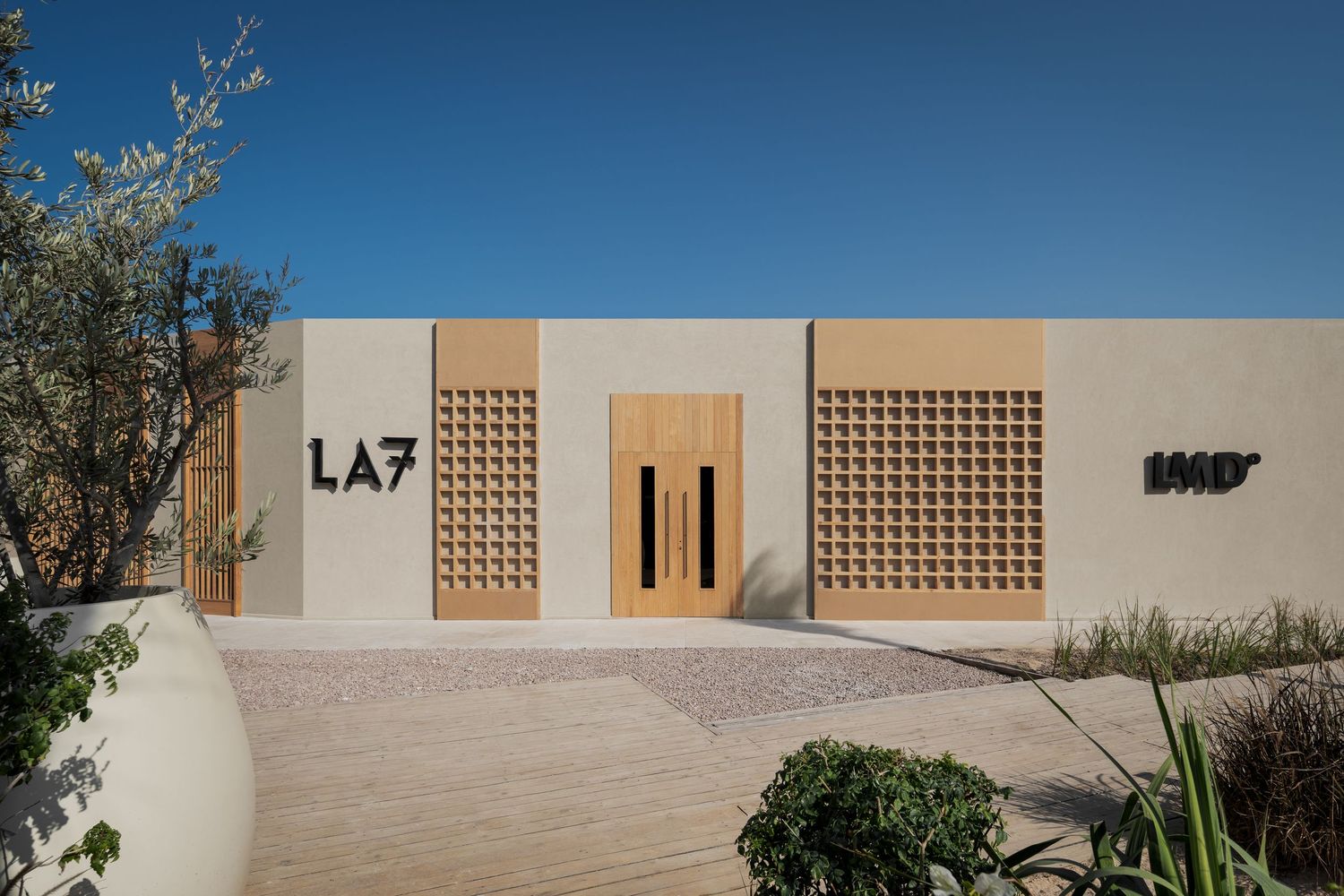LA7 modern boutique exterior with geometric wooden facade details, large entrance door, and desert landscaping.