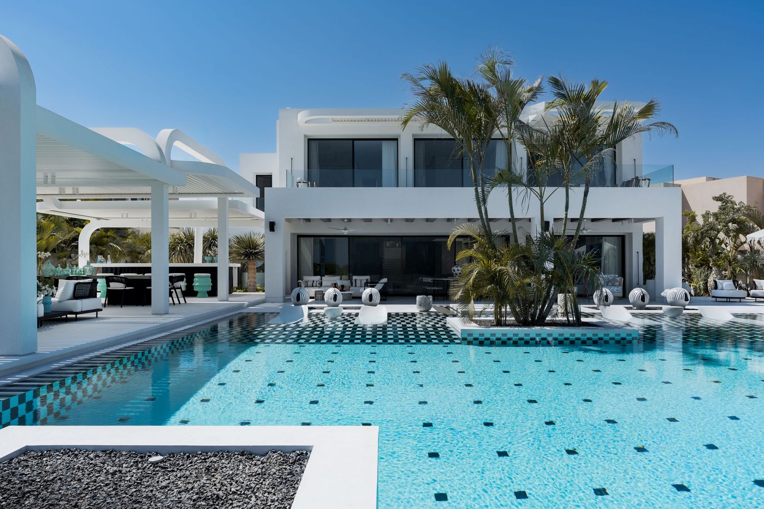 Modern luxury villa with large swimming pool featuring black and white tile details and lush palm trees.