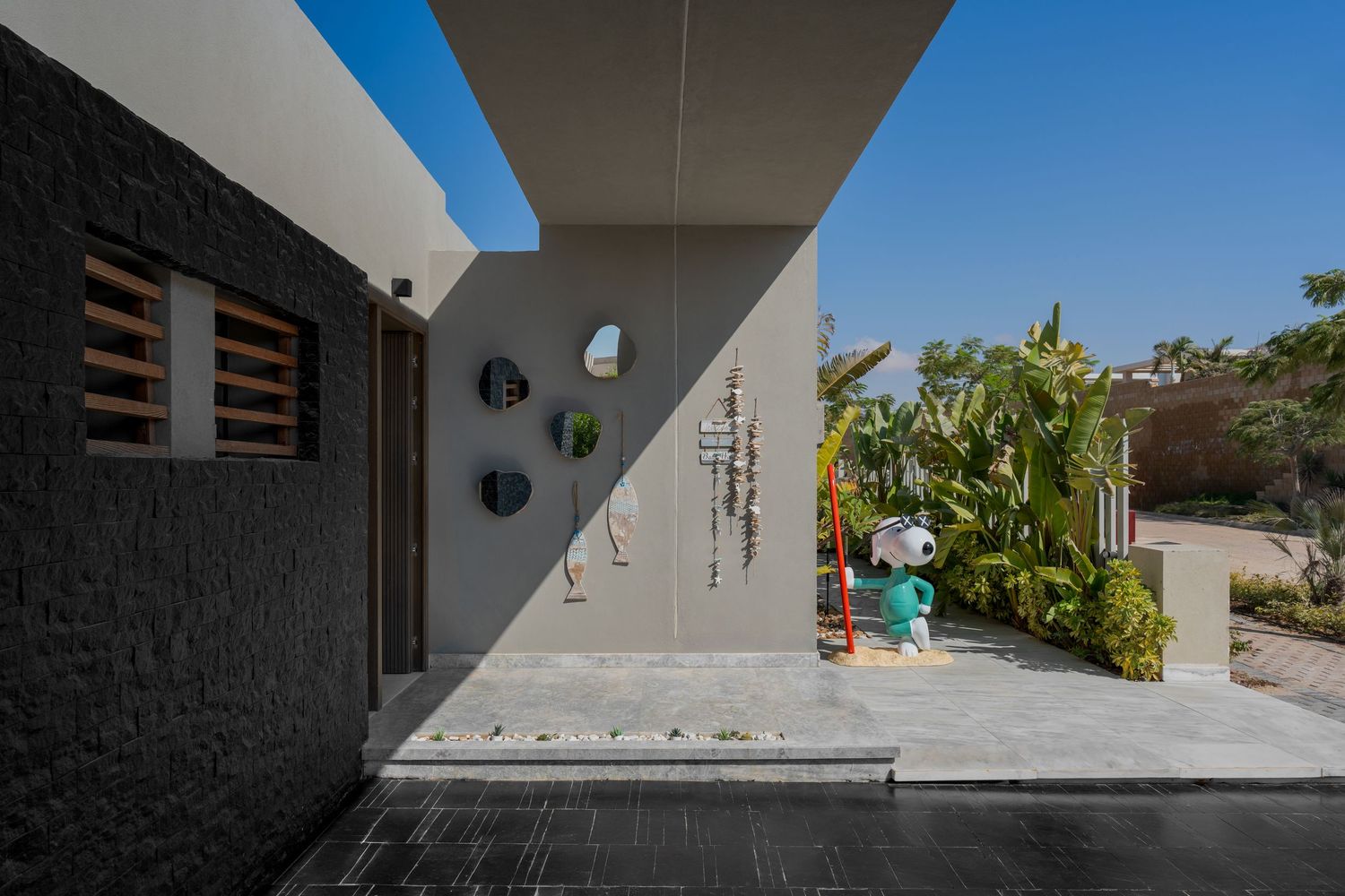 Modern home entrance with Snoopy sculpture, decorative wall art, and lush tropical landscaping.