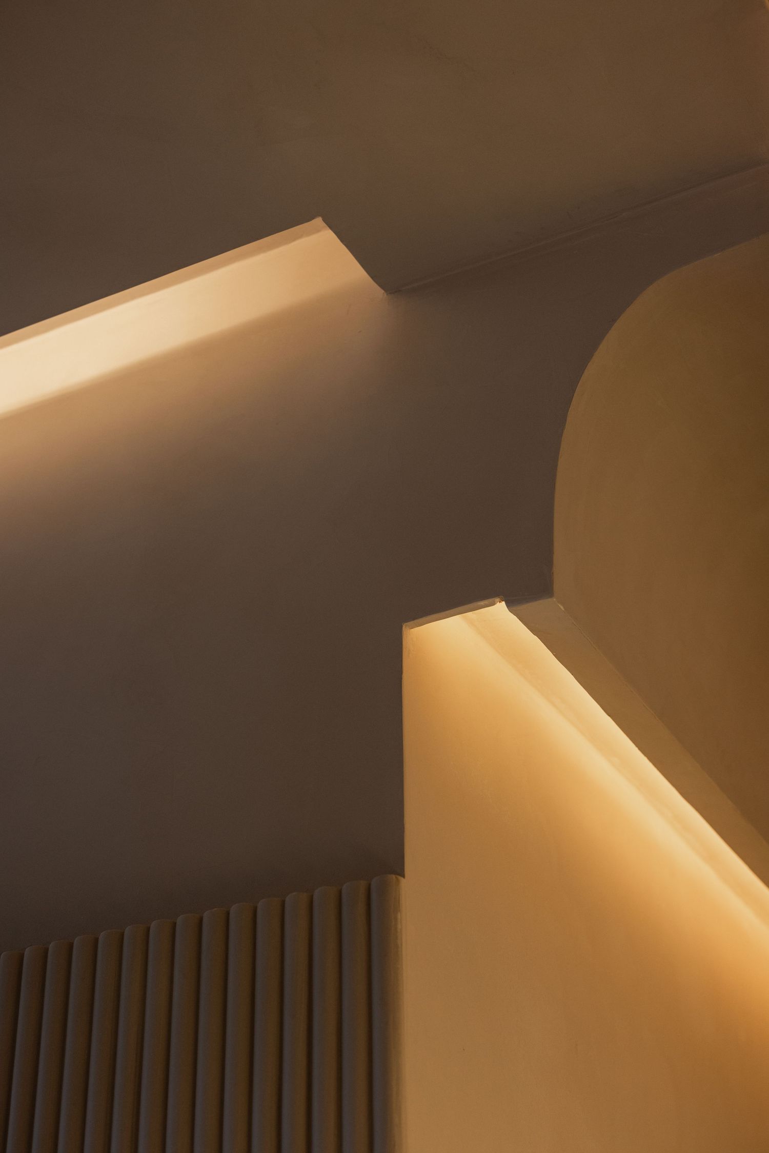 Warm LED cove lighting highlights curved archway and slatted wall panels in a luxury beige interior space.