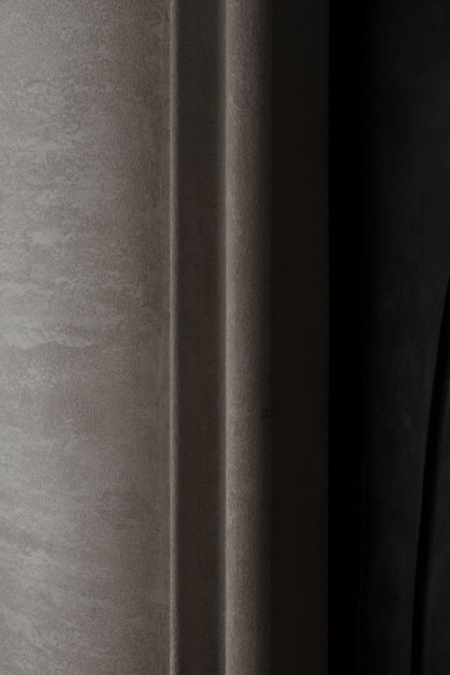Close-up of textured taupe wall panel with dark curtain in modern interior design.