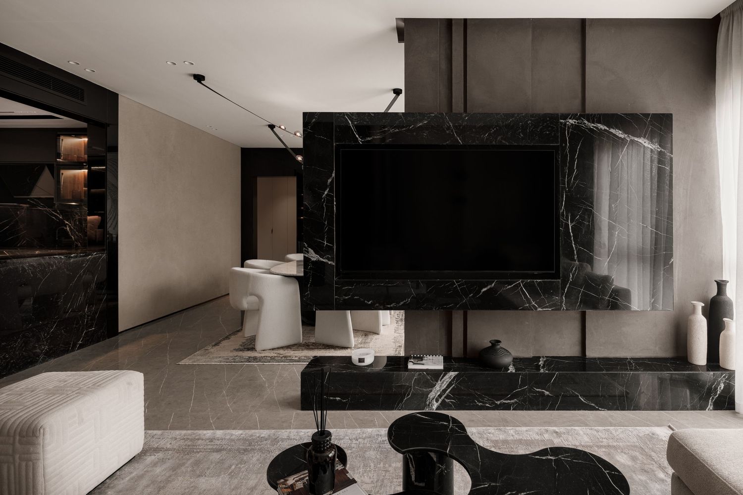 Contemporary living room featuring black marble TV wall, gray sofa, and dark sculptural furniture pieces.