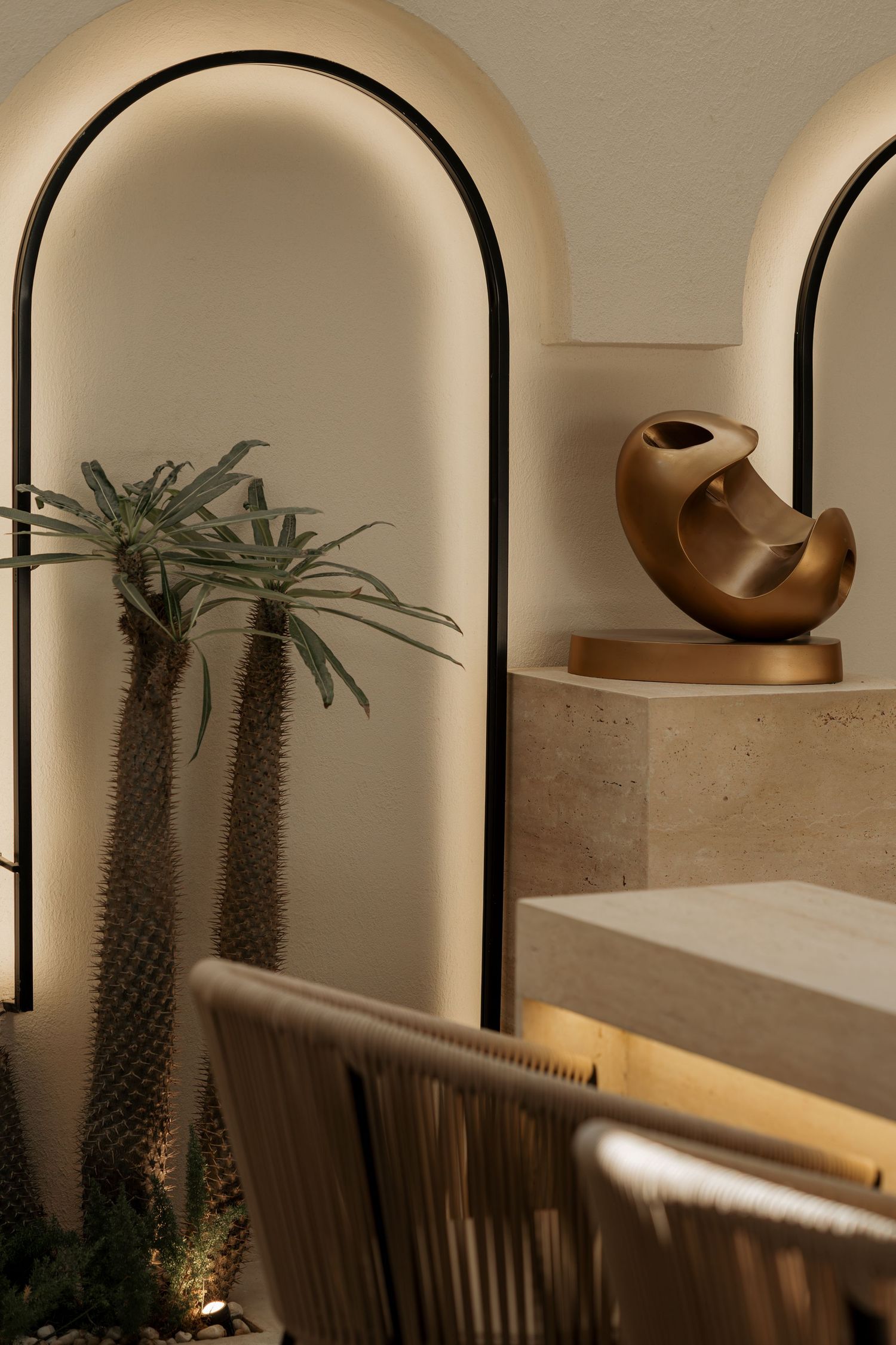 Illuminated arched wall niches with desert plants and a bronze sculptural decor piece on a travertine pedestal.