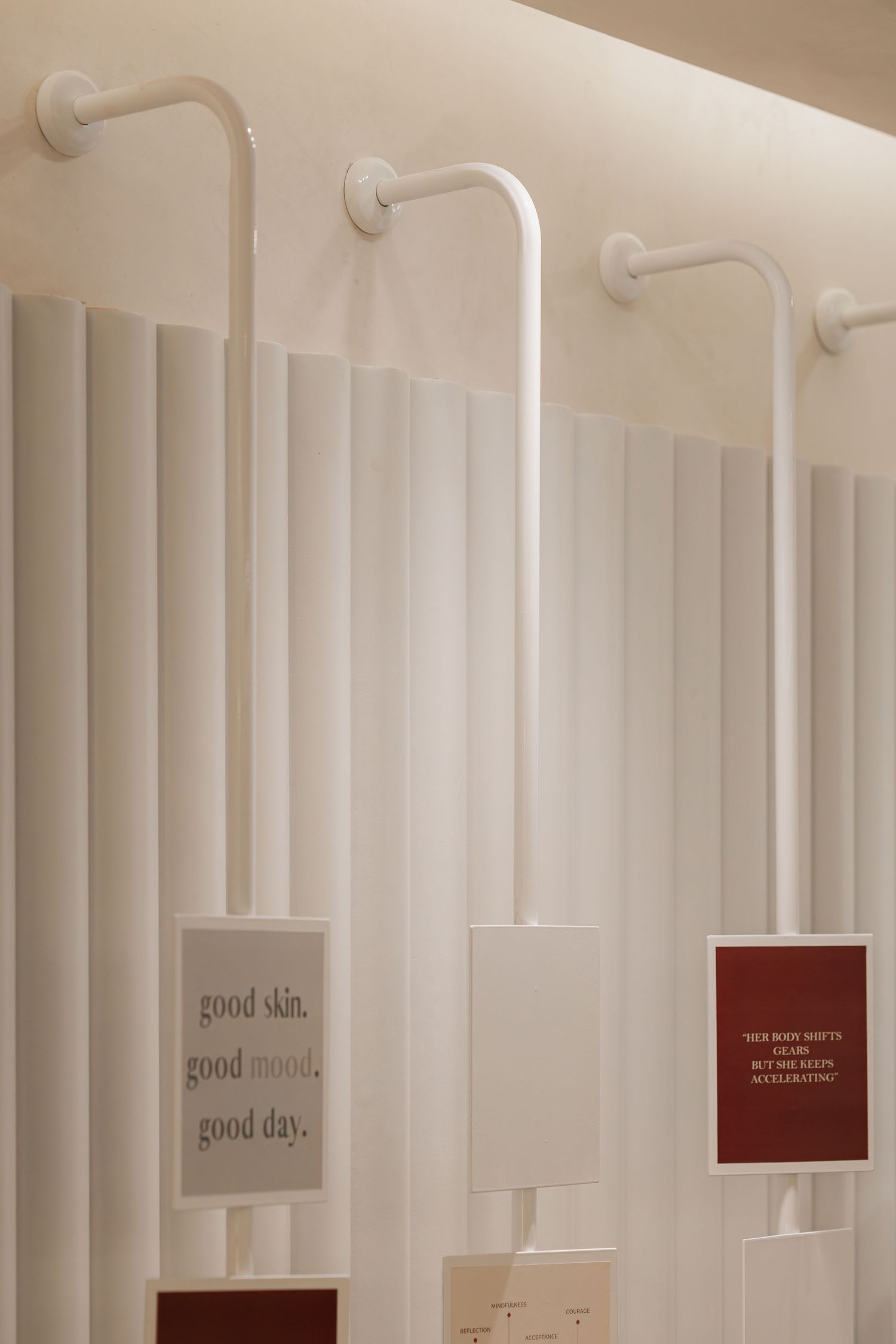 White fluted wall display with curved arm fixtures holding motivational skincare quote cards in a modern beauty studio.