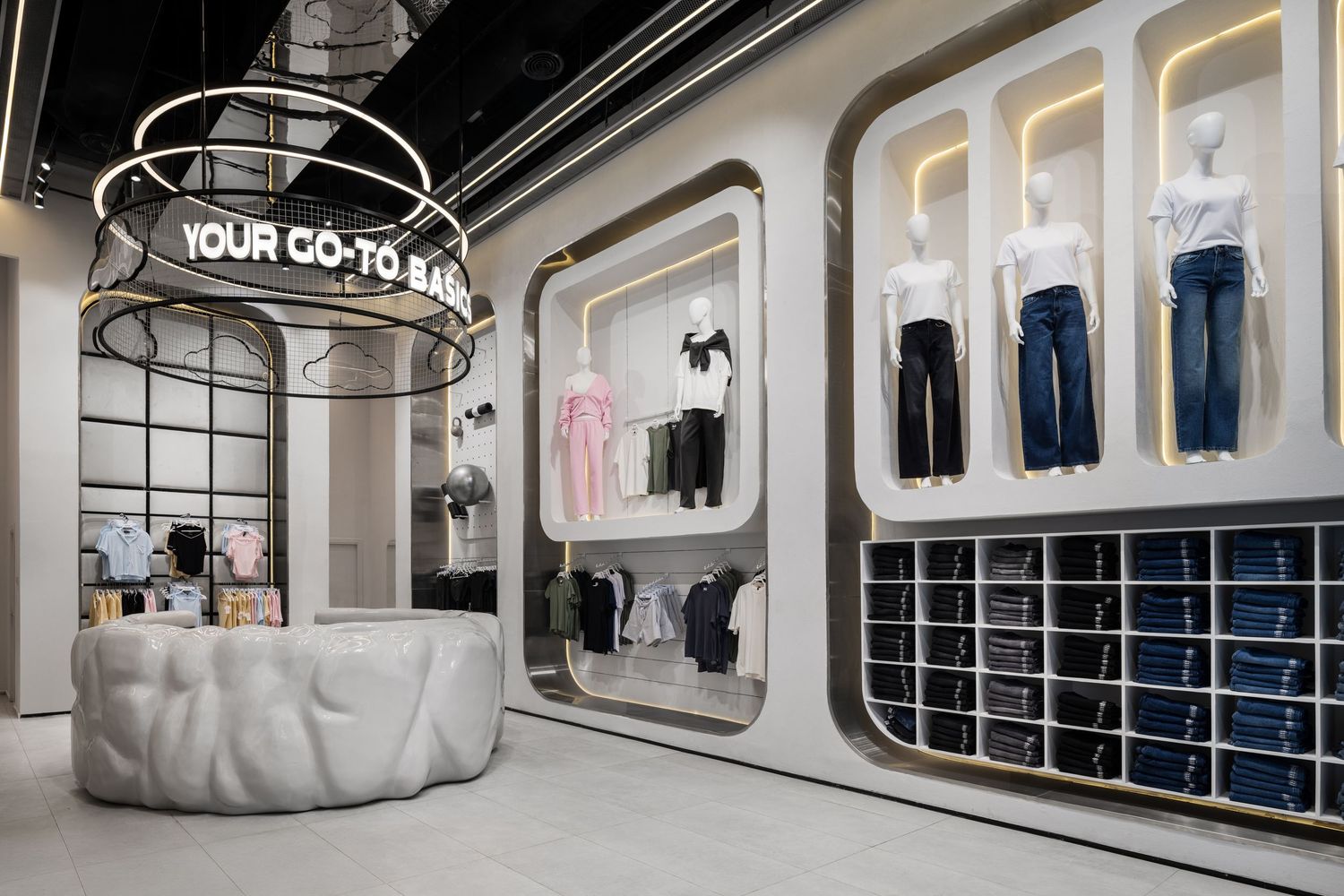 Bright fashion boutique with YOUR GO-TO BASICS sign, jeans wall display, and sculptural counter.