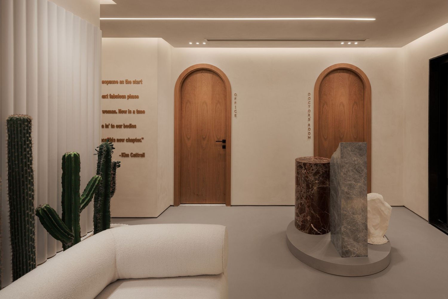 Contemporary retail space with arched wooden doors, sculptural stone pedestals, cactus decor, and inspirational wall text.