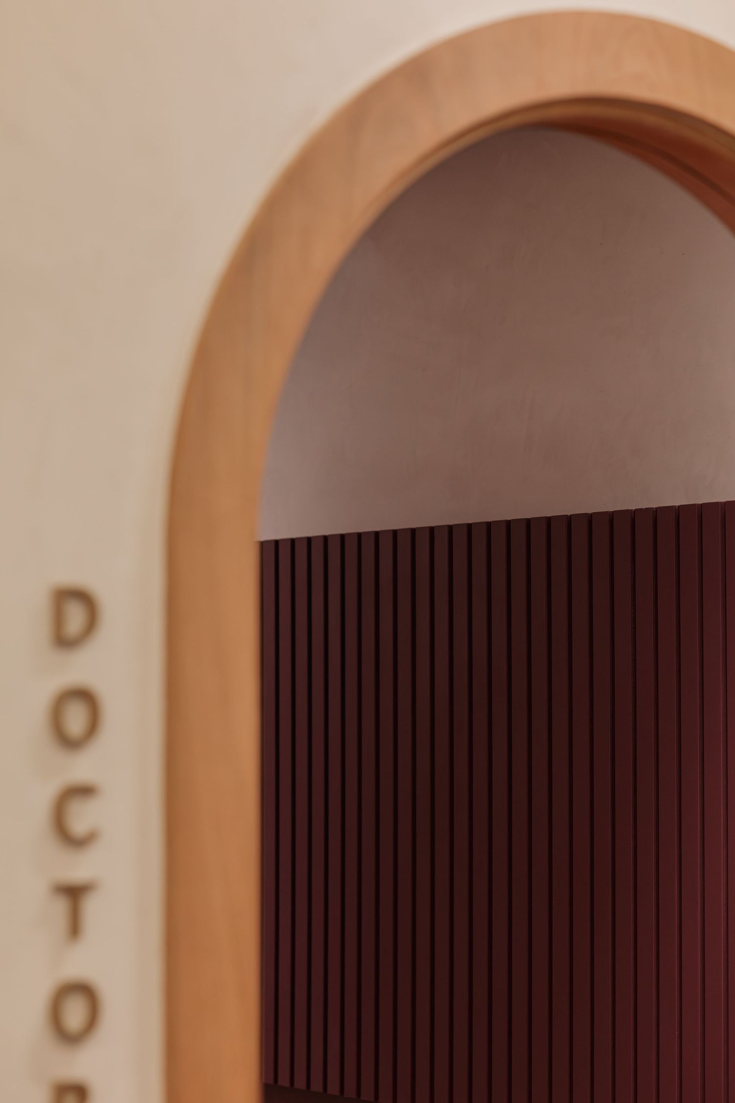 Close-up of warm wooden arched doorway with burgundy vertical slat wall panel and partial DOCTOR text signage.