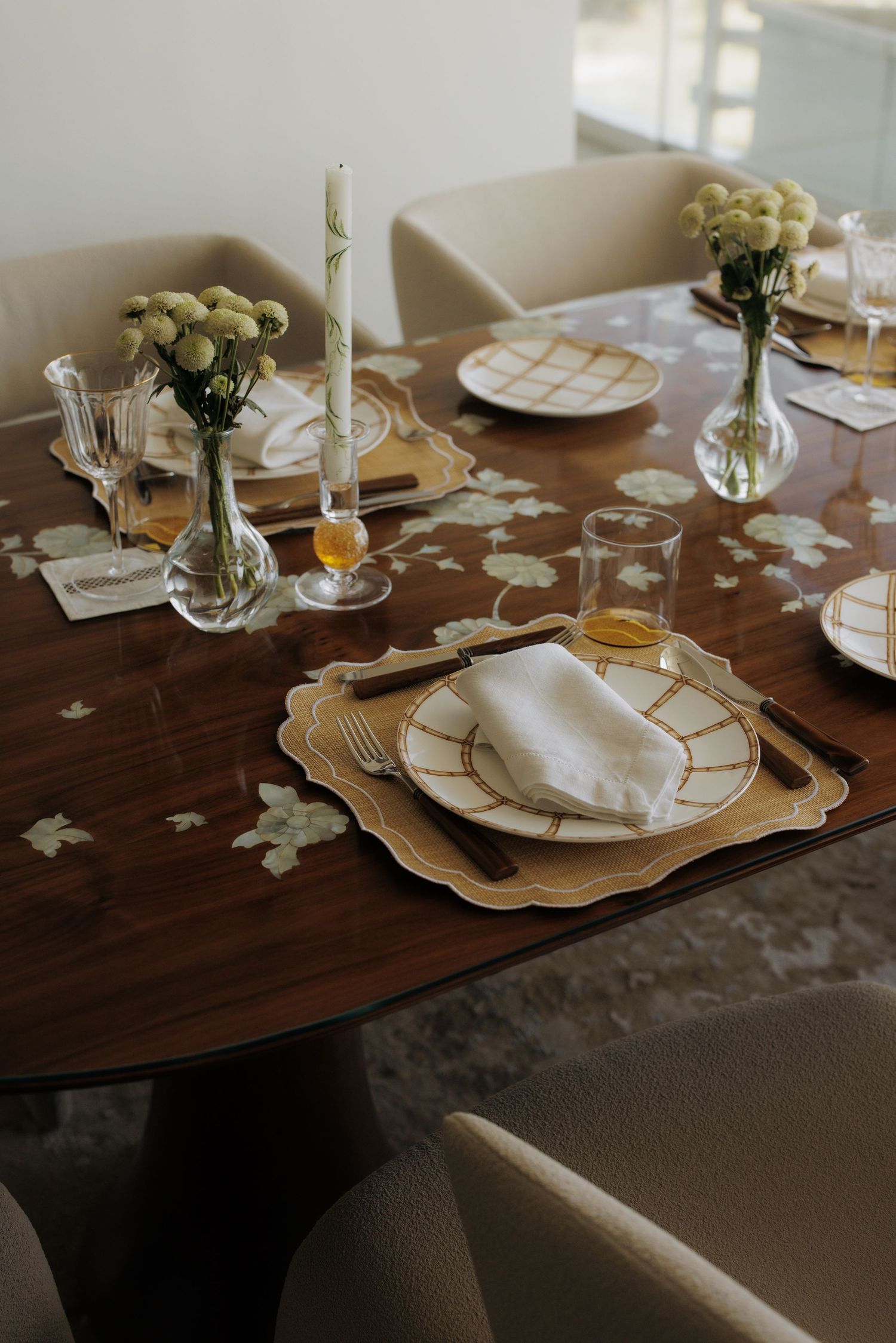 Beautifully styled oval dining table with gold-trimmed plates, candles, and fresh floral arrangements.