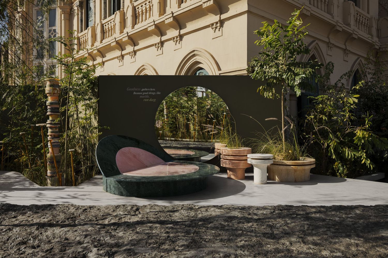 Green marble sculptural daybed with pink cushion displayed against ornate building facade outdoors.