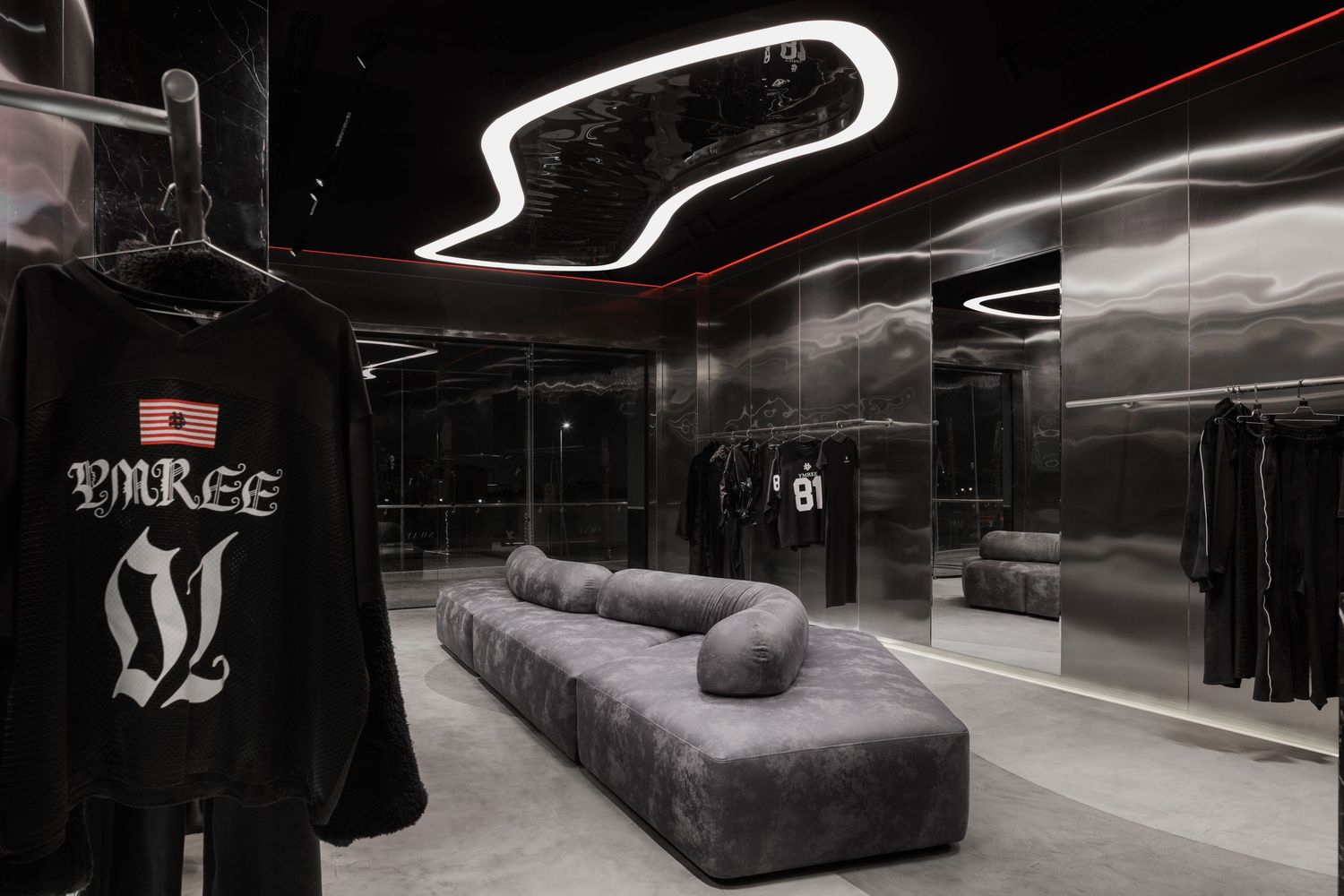 Modern dark fashion boutique with YMREE branded black sweatshirt display, gray velvet sofa, and sculptural white LED ceiling light.