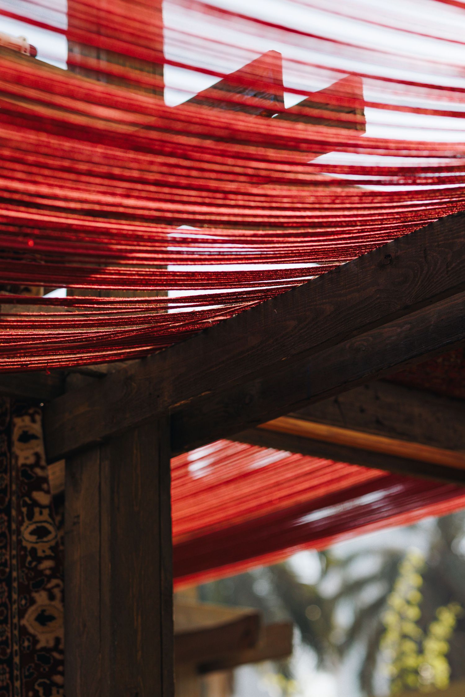 Close-up of vibrant red threads stretched across wooden beams of a traditional textile weaving structure.